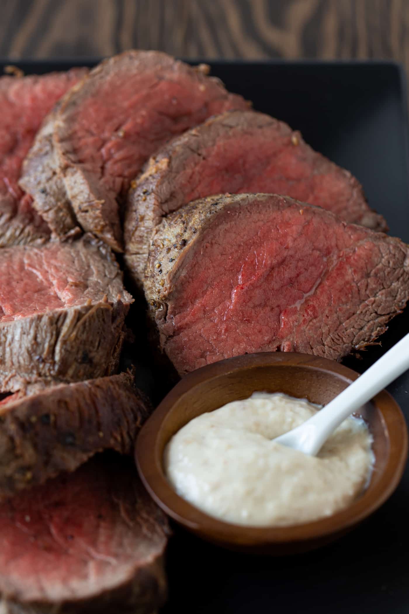 sliced beef tenderloin on platter with horseradish sauce.