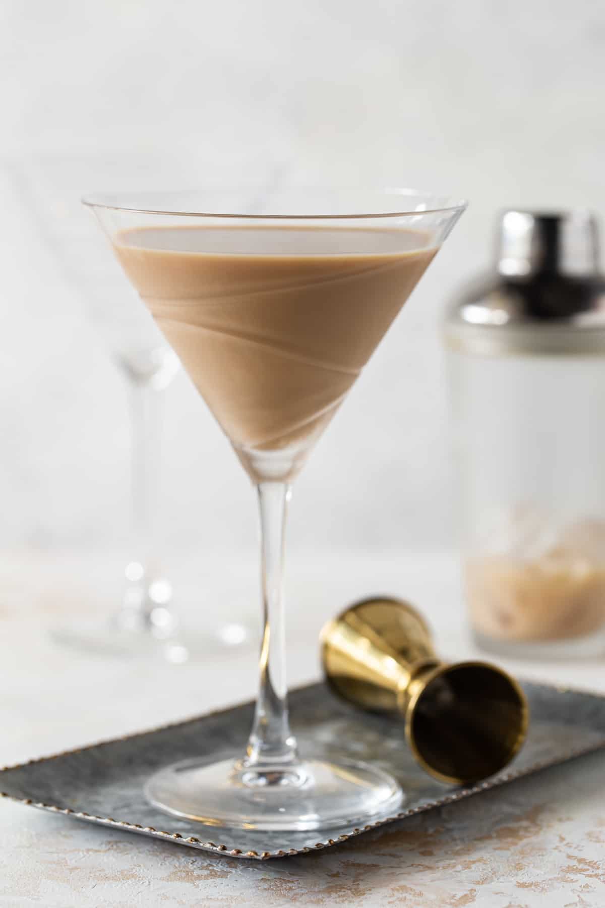 single martini glass filled with dark drink on white background with gold shot glass