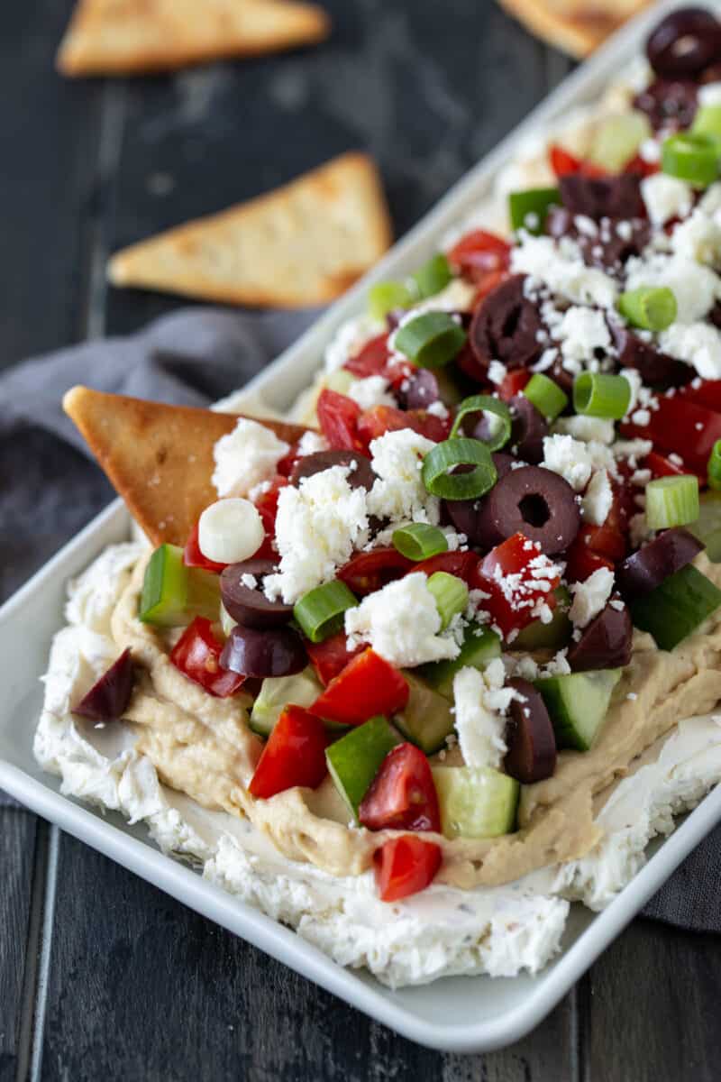 White platter filled with Layered Greek Dip and pita chips. 