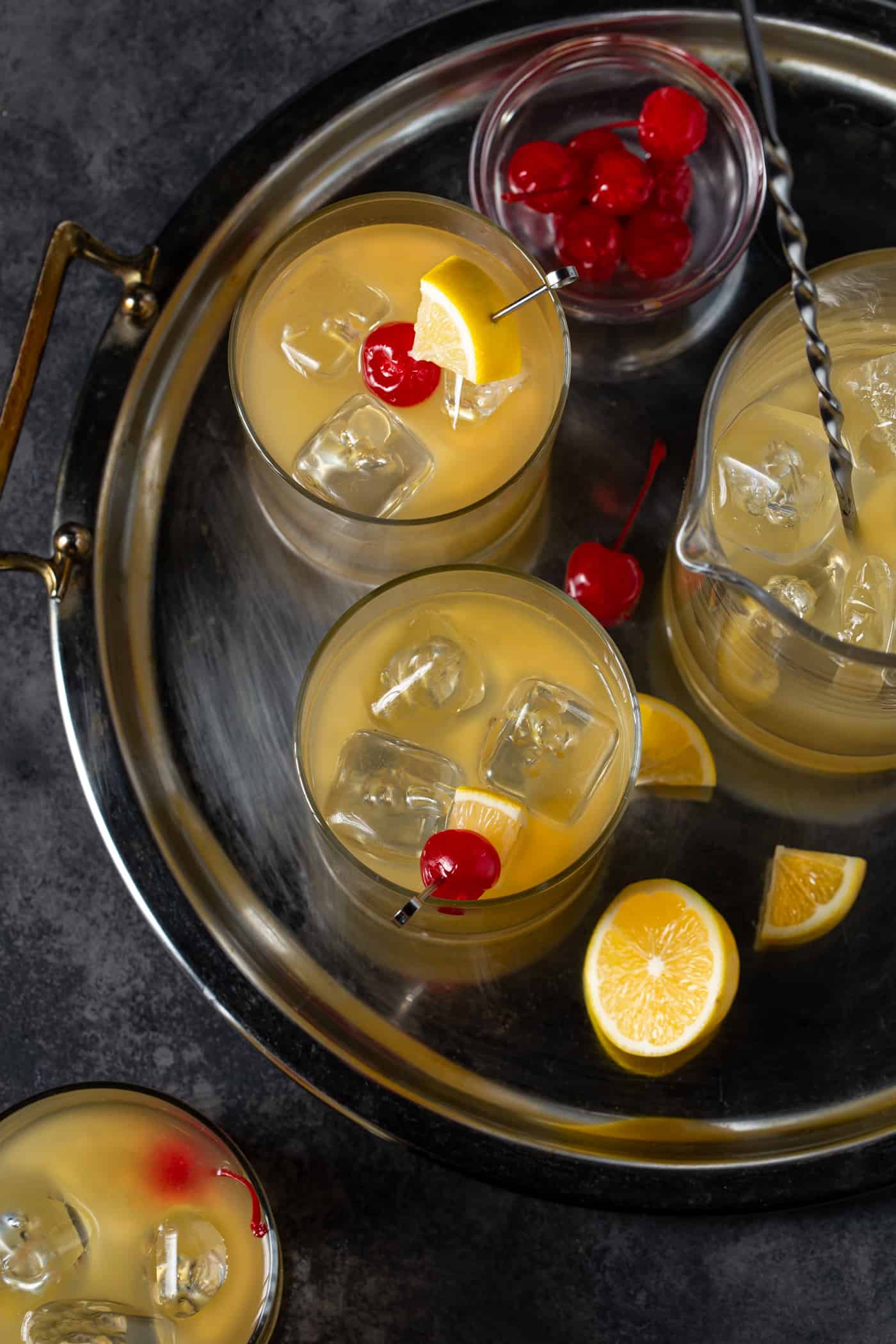 Platter filled with glasses of Whiskey Sours. Garnished with maraschino cherries and Meyer lemon slices. 