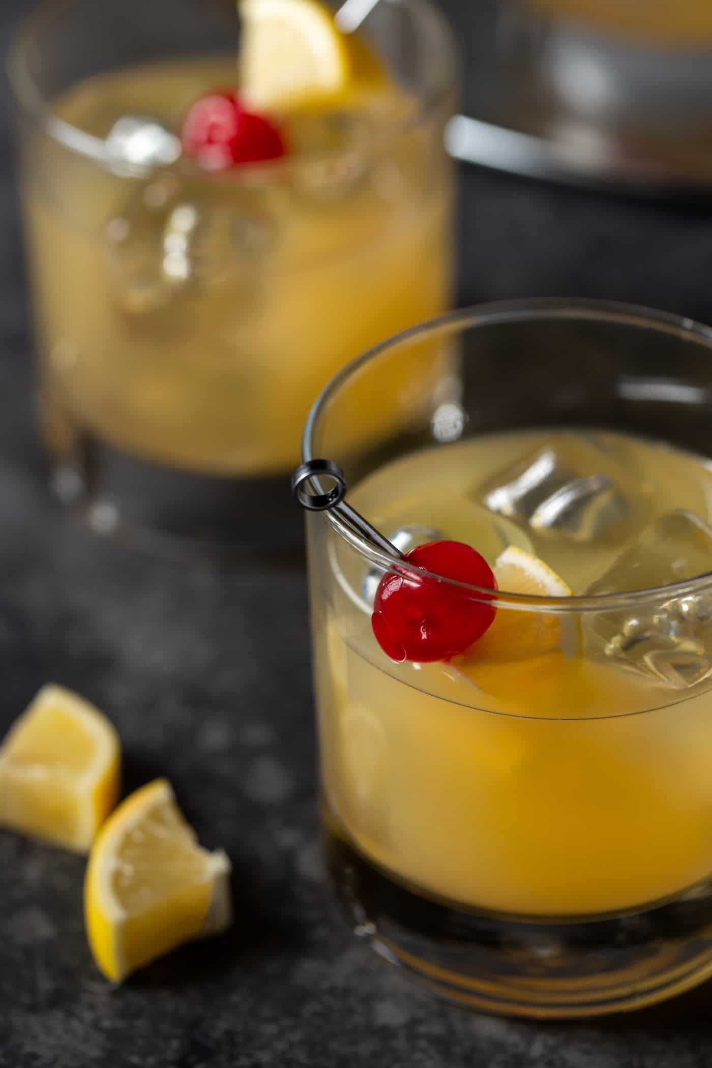 Two lowball glasses filled with cocktails and garnished with maraschino cherries and Meyer lemon slices.