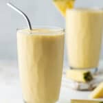 Two tall glasses filled with Mango Pineapple Smoothies and garnished with fresh pineapple wedges.