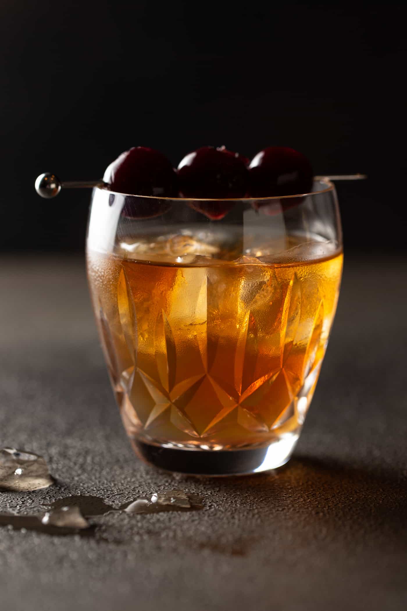 Low ball old fashioned glass filled with manhattan cocktail and garnished with a skewer of cherries.