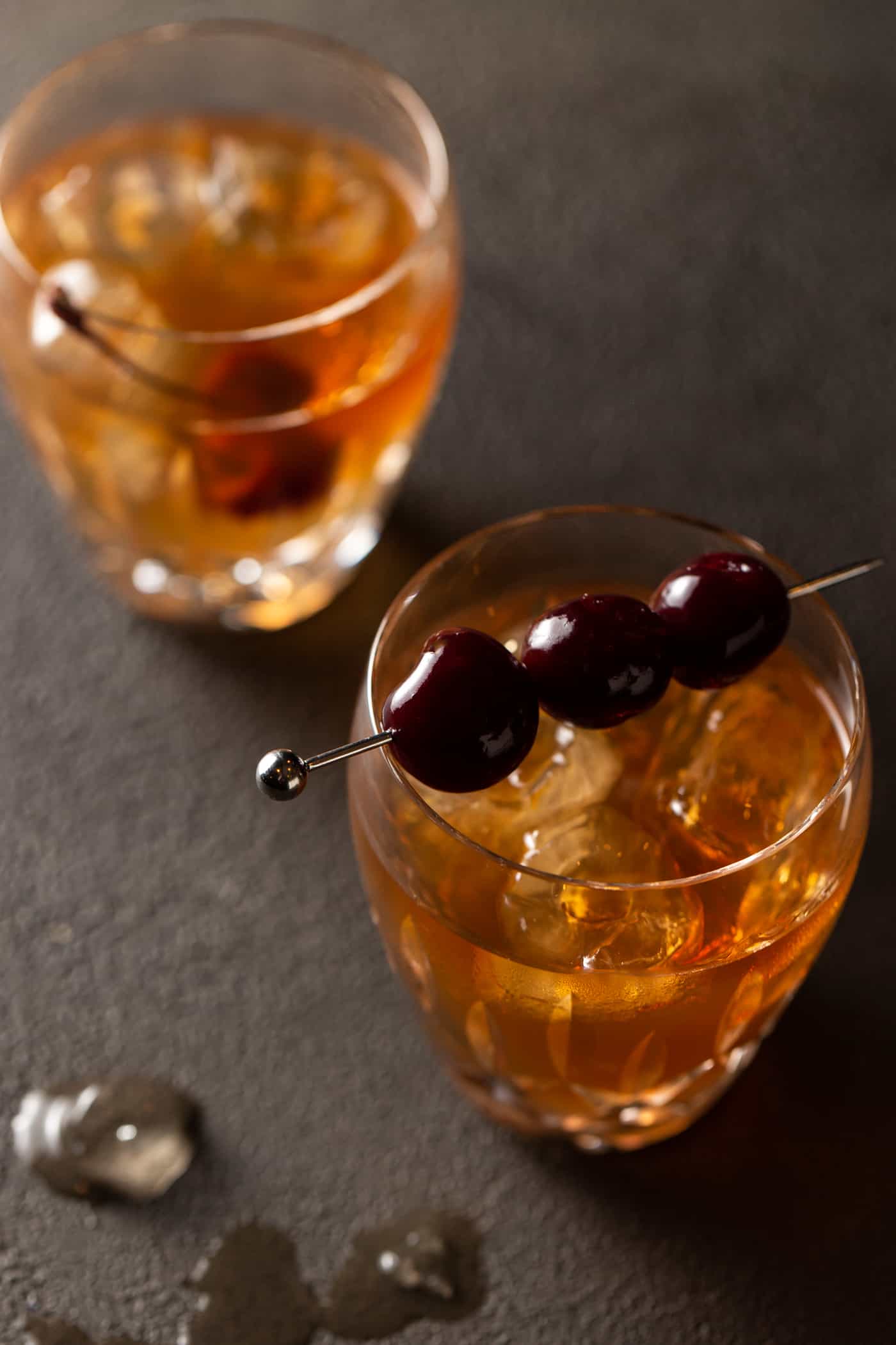 A glass cup on a table, with Manhattan and cherries.