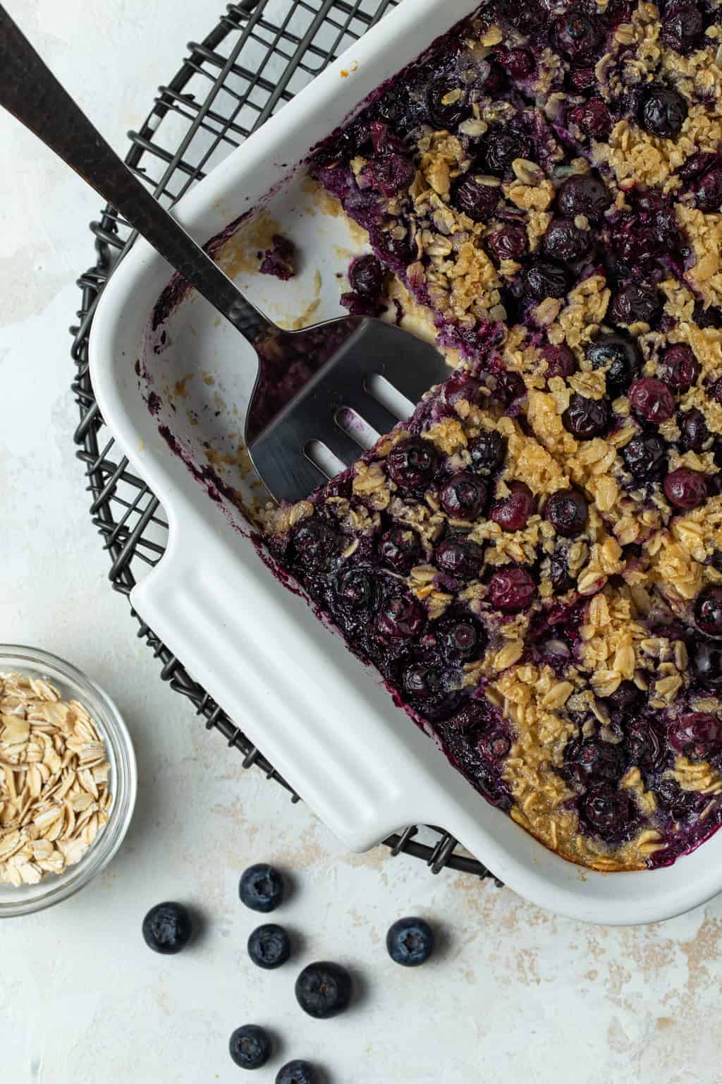 Top down image of blueberry baked oatmeal in a white baking dish cut into squares with one piece removed from the pan.