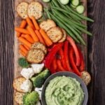 Wooden cutting board filled with vegetables, crackers and a bowl filled with a healthy Avocado Dip that is made with Greek yogurt