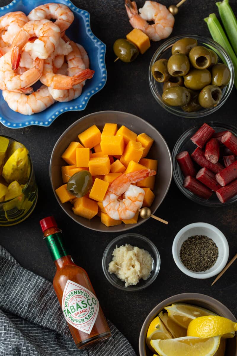 various small bowls with different garnishes including shrimp, olives, beef sticks, pickles, cheese cubes, horse radish, pepper, and Tabasco sauce