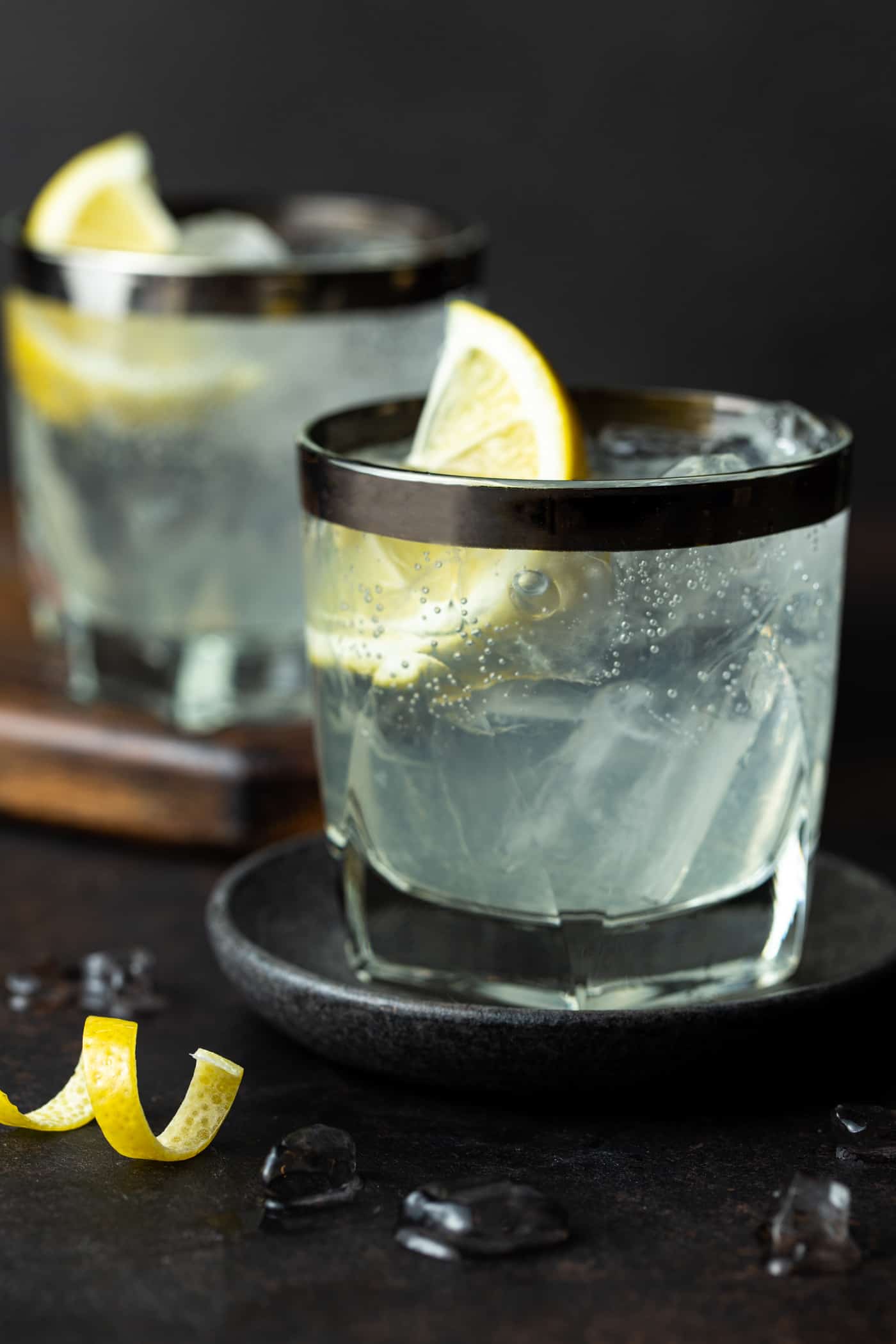 Two lowball glasses filled with Elderflower Vodka Sodas. Garnished with fresh lemon wedges and a lemon peel twist.