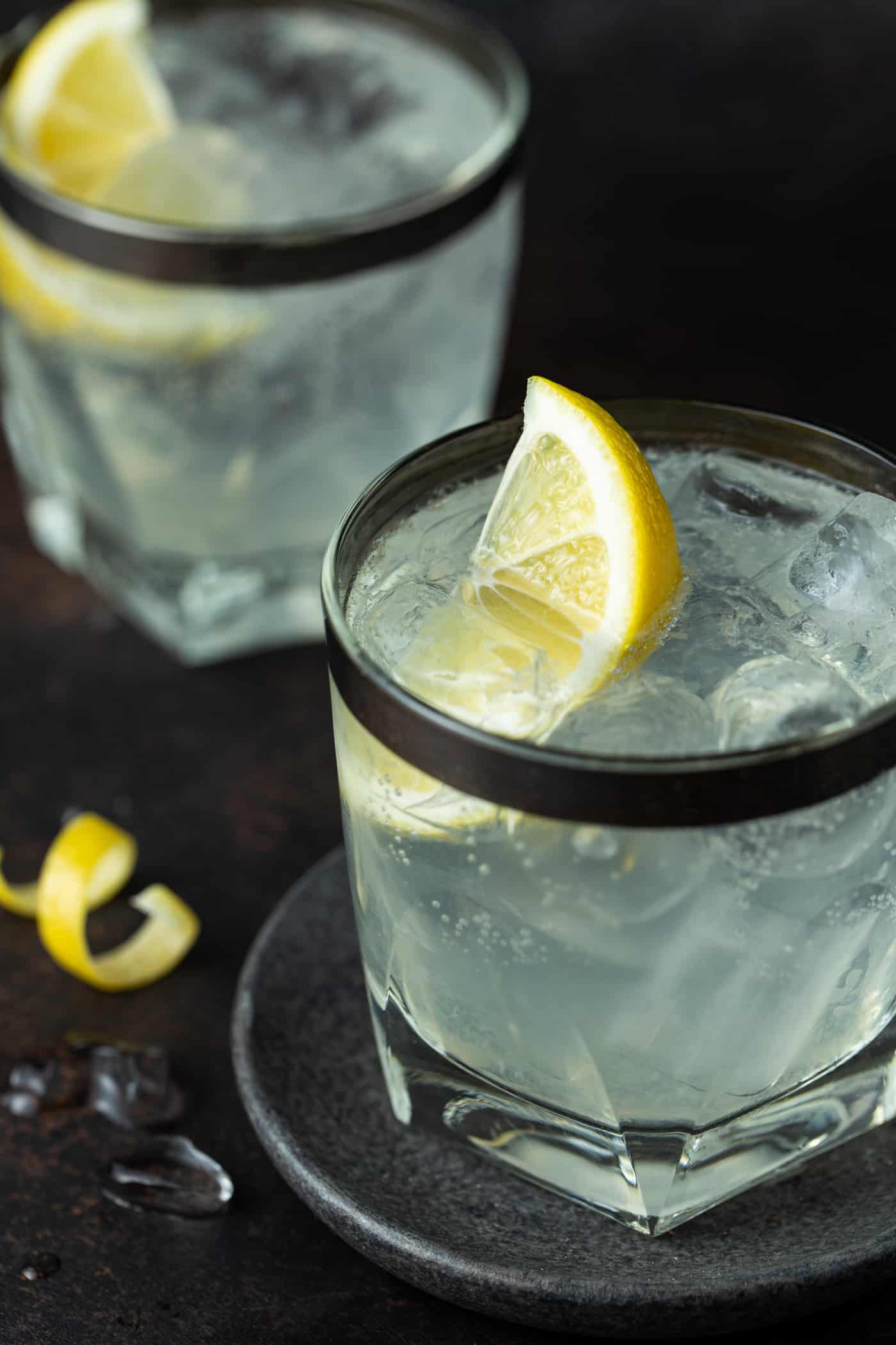 Two lowball glasses filled with Vodka Soda, with fresh lemon wedges.