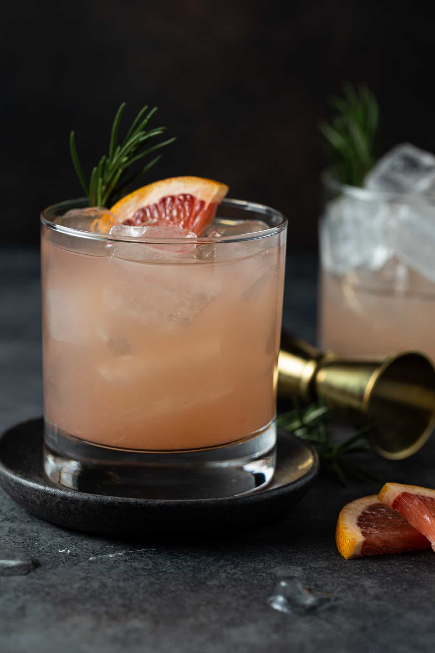 drinks in low ball glasses on dark gray coasters with fresh grapefruit for a garnish.