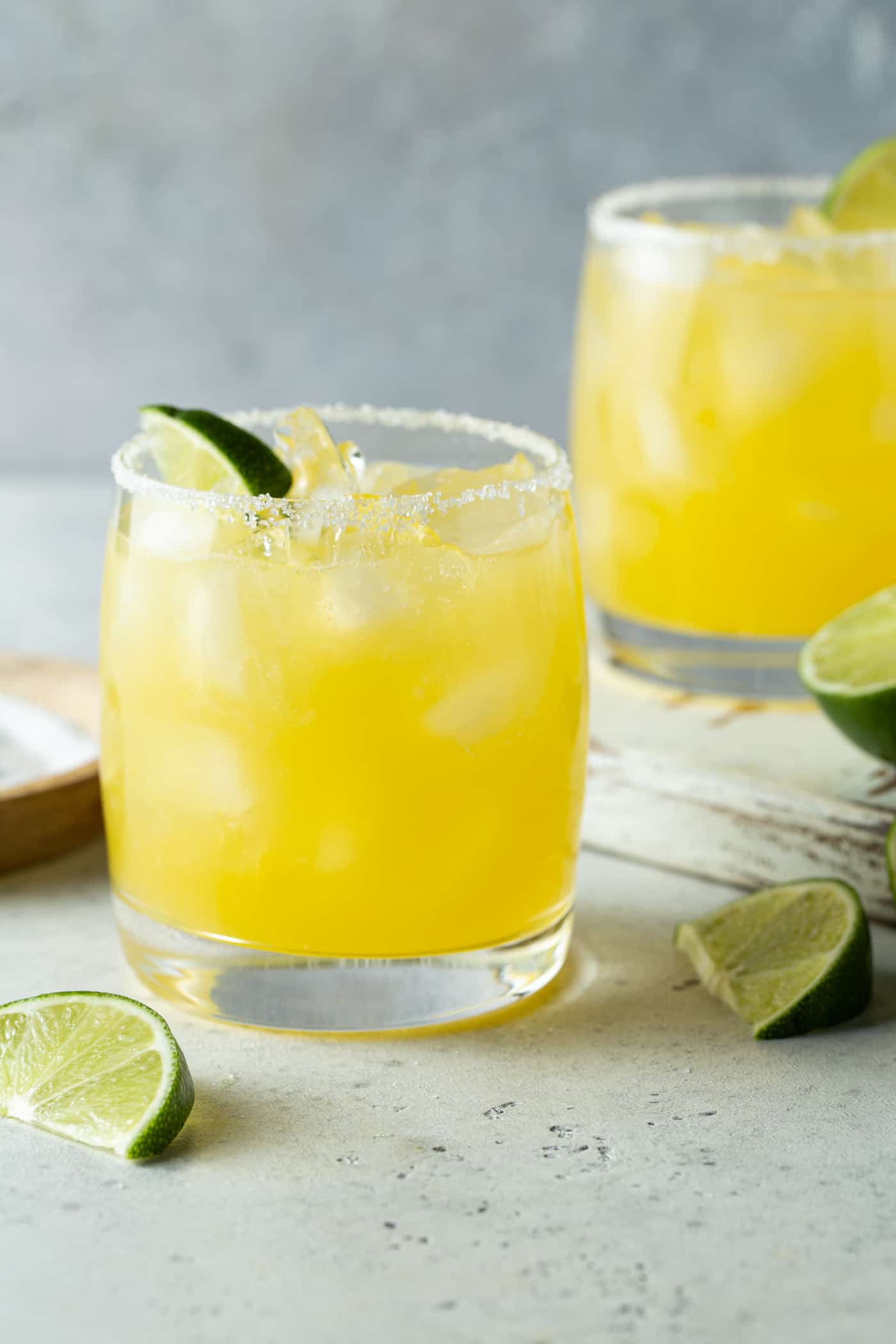 Two lowball glasses of mango margarita. Garnished with fresh lime wedges.