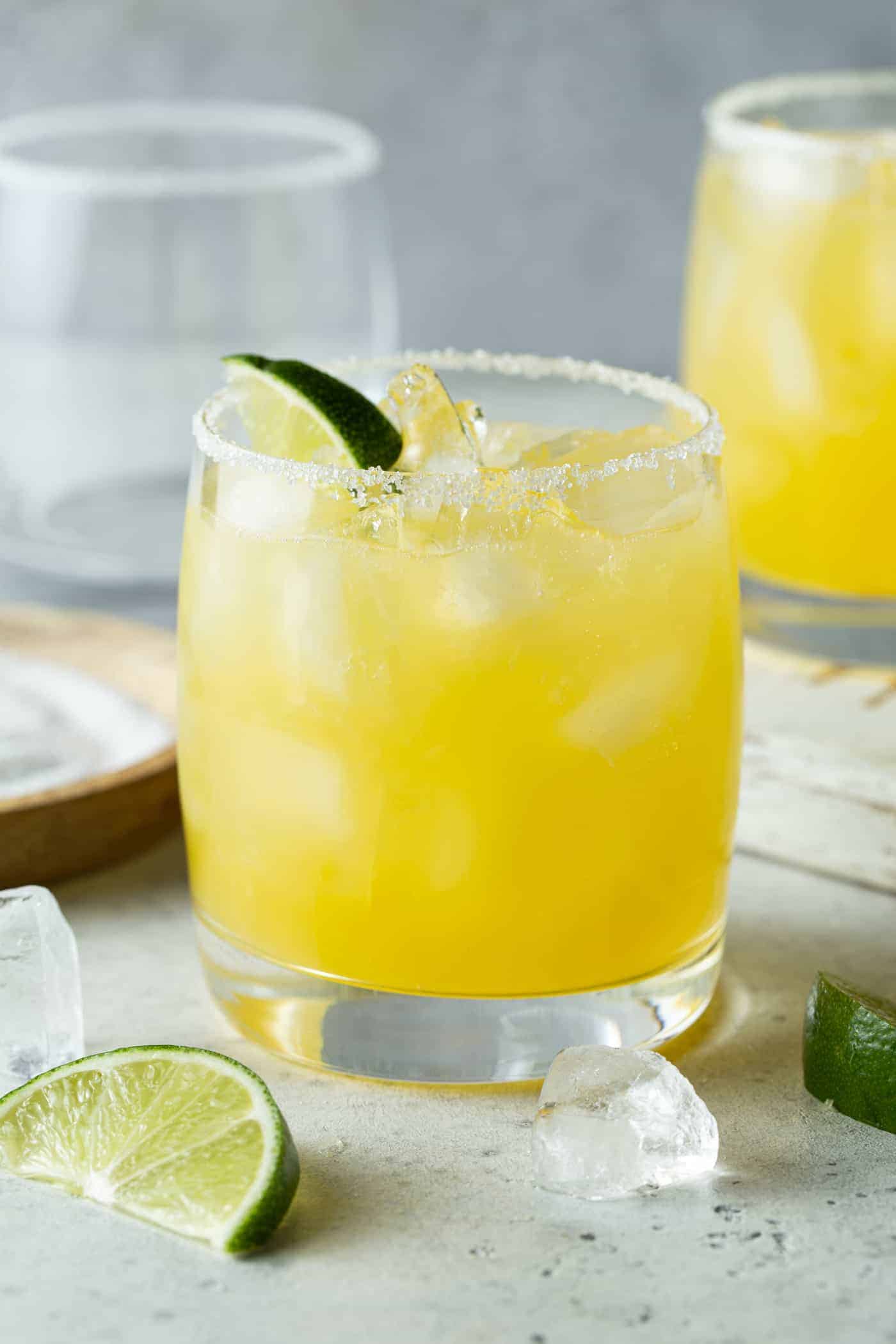 Lowball glass filled with mango margarita and garnished with a fresh lime wedge.