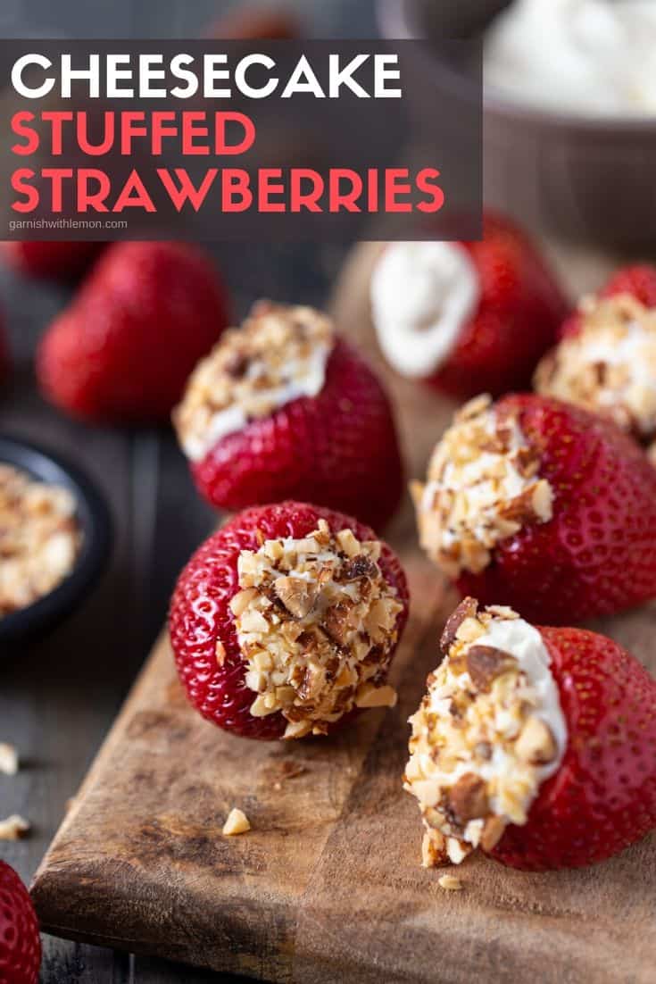 Strawberries lying on a wood cutting board that are filled with cheesecake filling and topped with chopped almonds