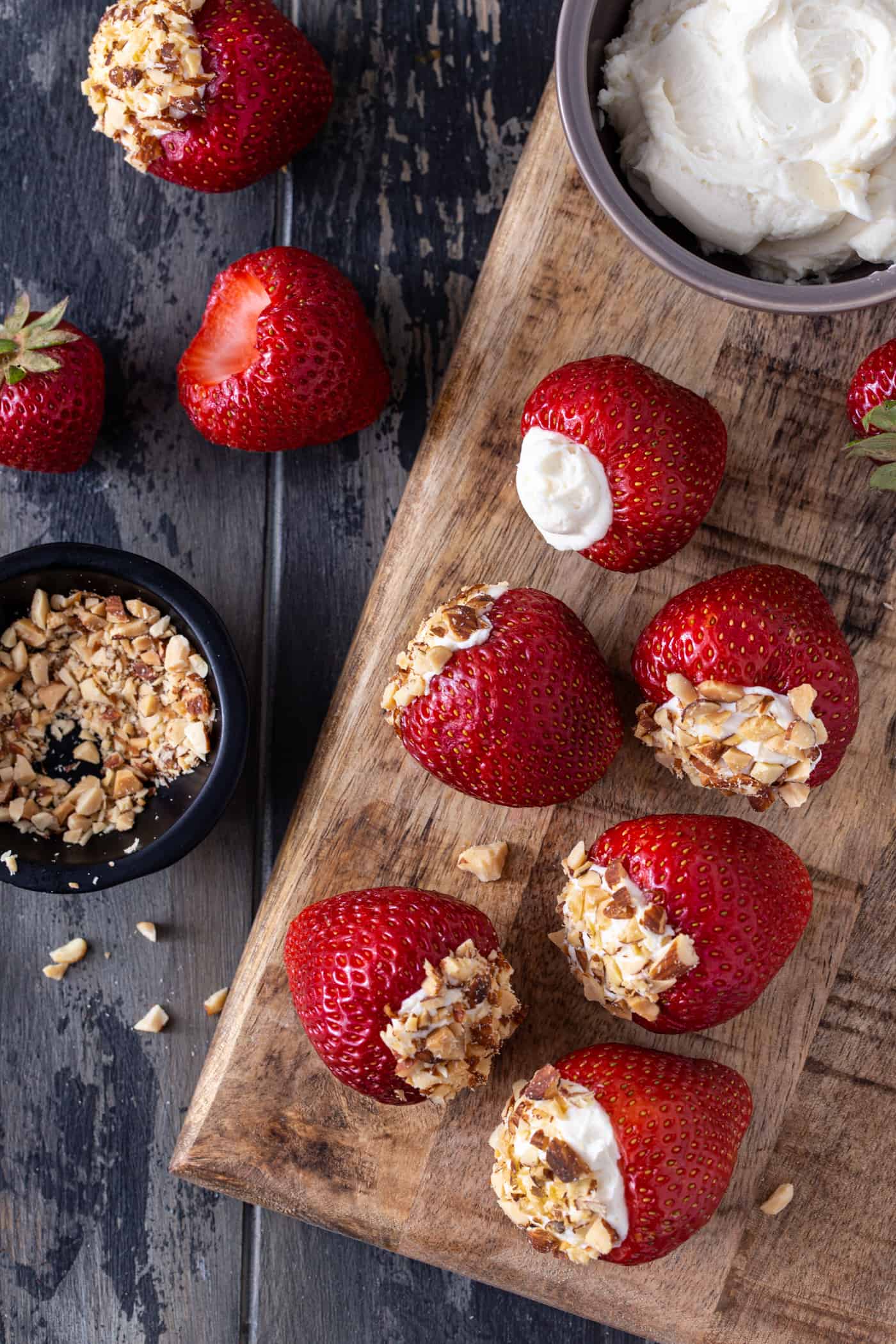 Strawberries on a wooden board stuffed with cheesecake filling and topped with crushed almonds