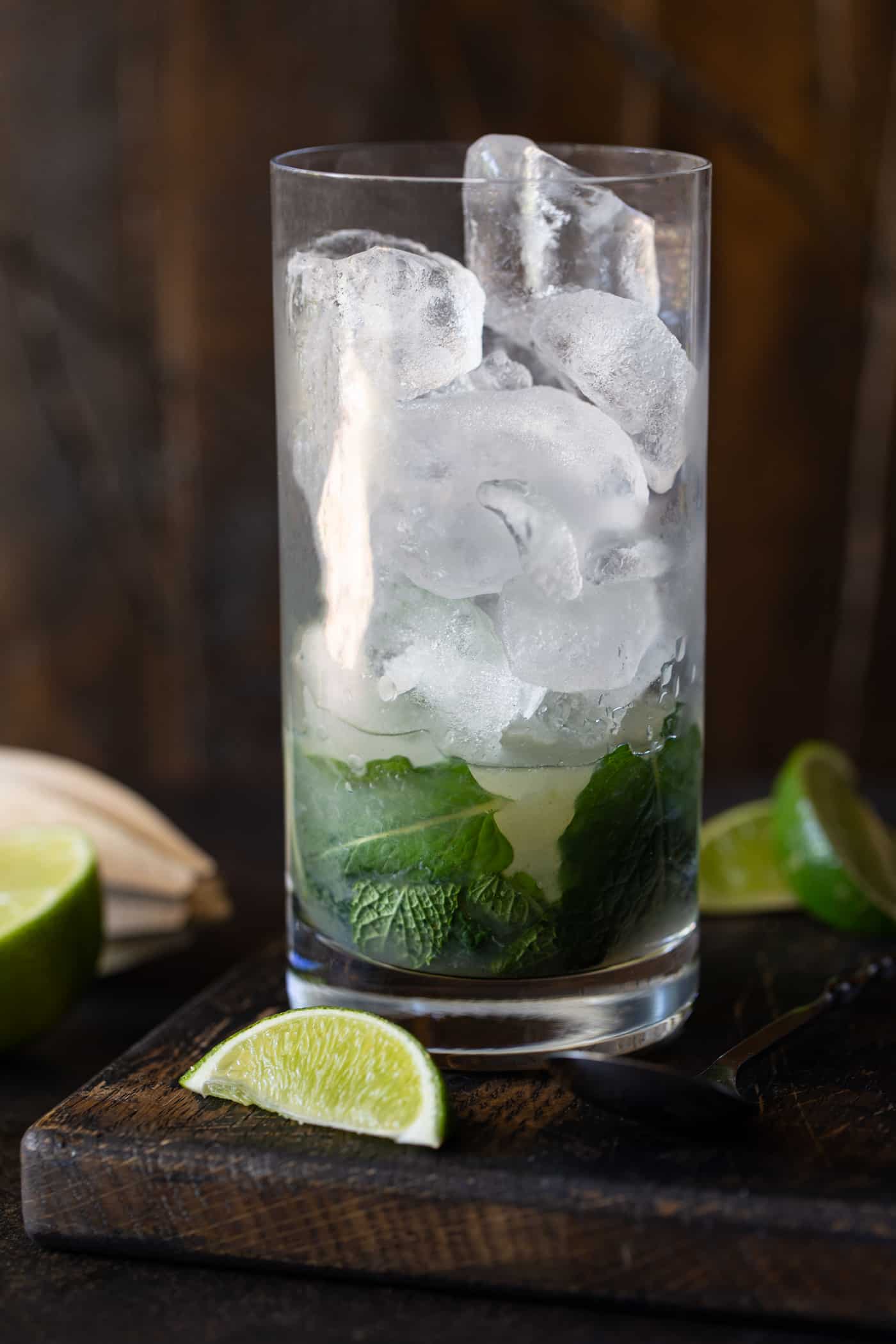 High ball glass with mint, sugar and lime muddled on bottom and filled with ice.