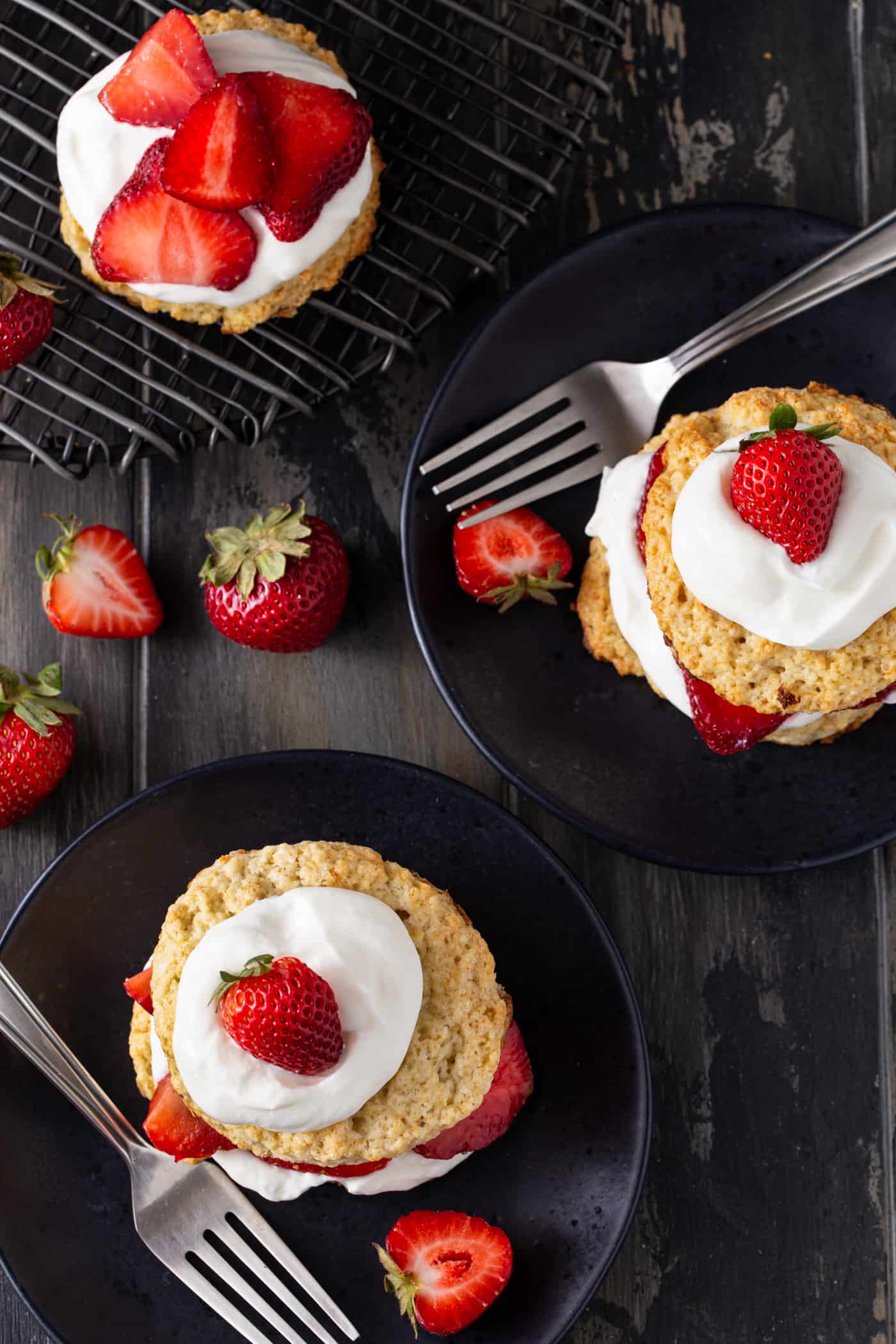 Strawberry shortcakes on black plates with forks and extra strawberries as garnish.