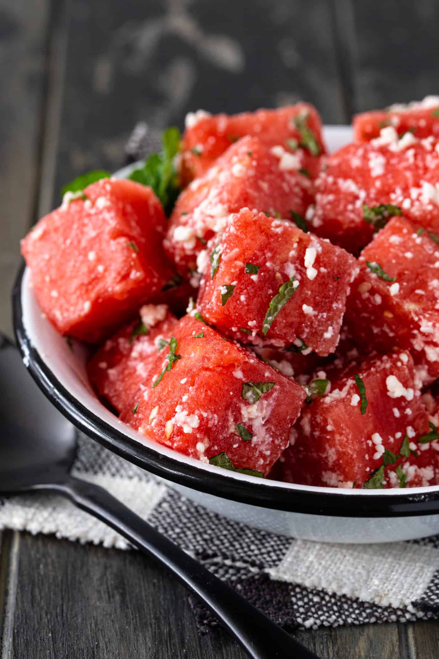 White bowl of watermelon feta salad on a black and white checkered napkin.