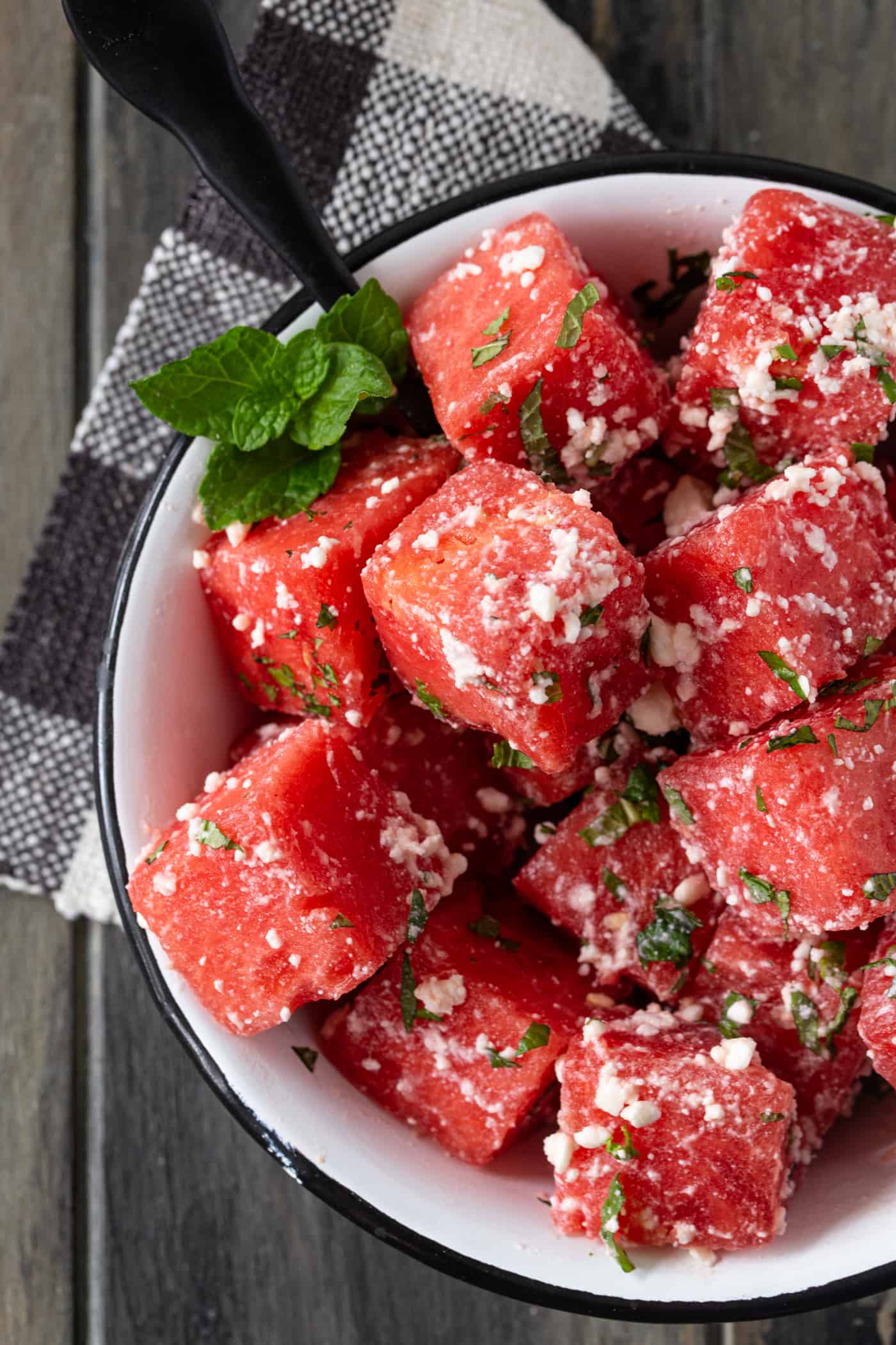White bowl with black rim filled with watermelon feta salad. Garnished with fresh mint.