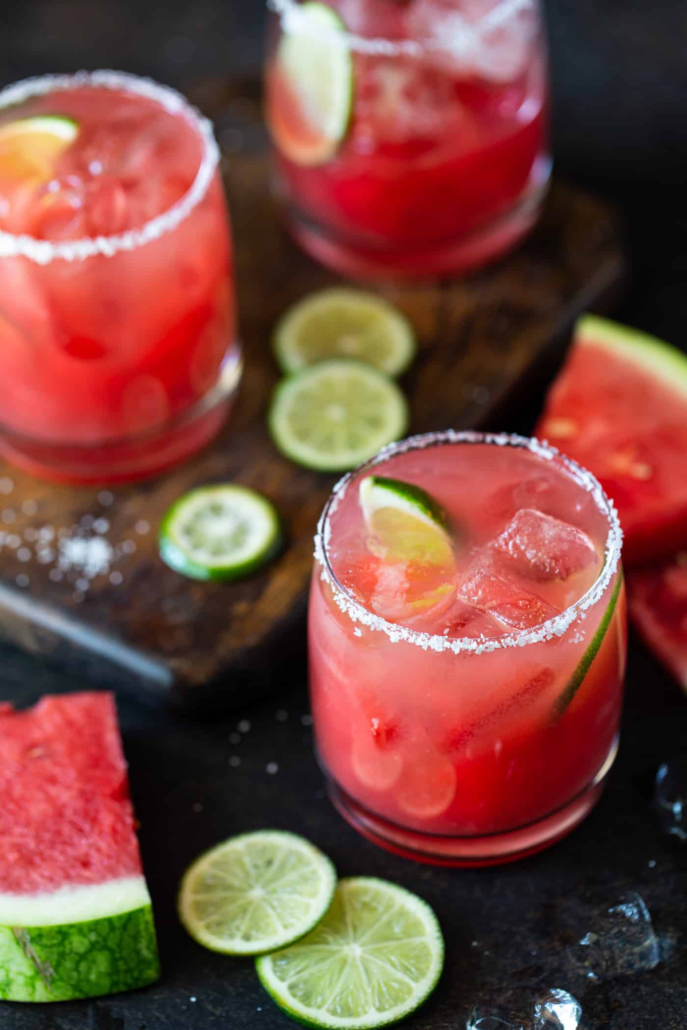 Lowball glasses with salted rims and filled with fresh watermelon margaritas on the rocks. Garnished with lime wheels and fresh watermelon chunks. 