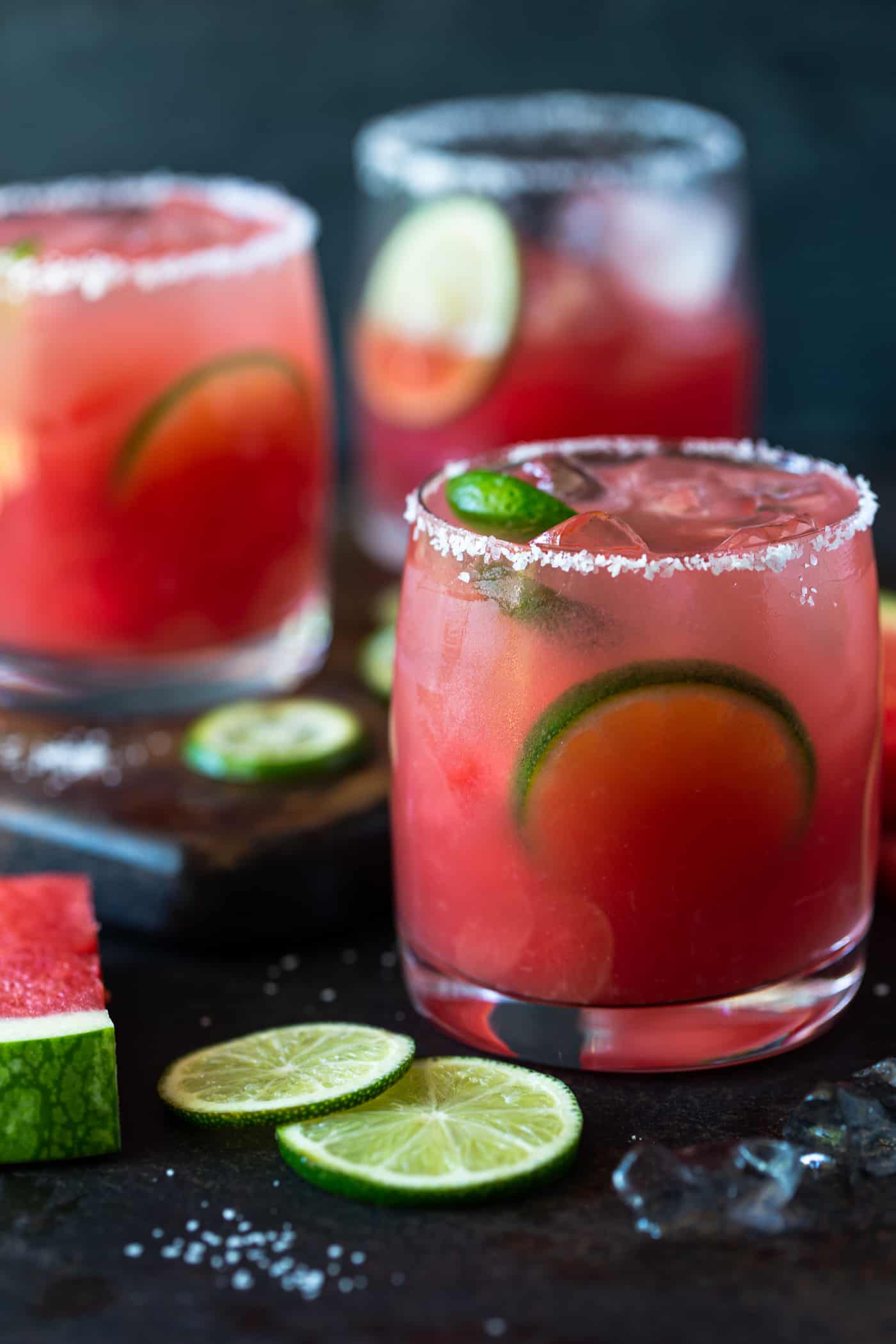 Lowball glasses rimmed with salt and filled with margaritas. Garnished with lime wheels and watermelon chunks.