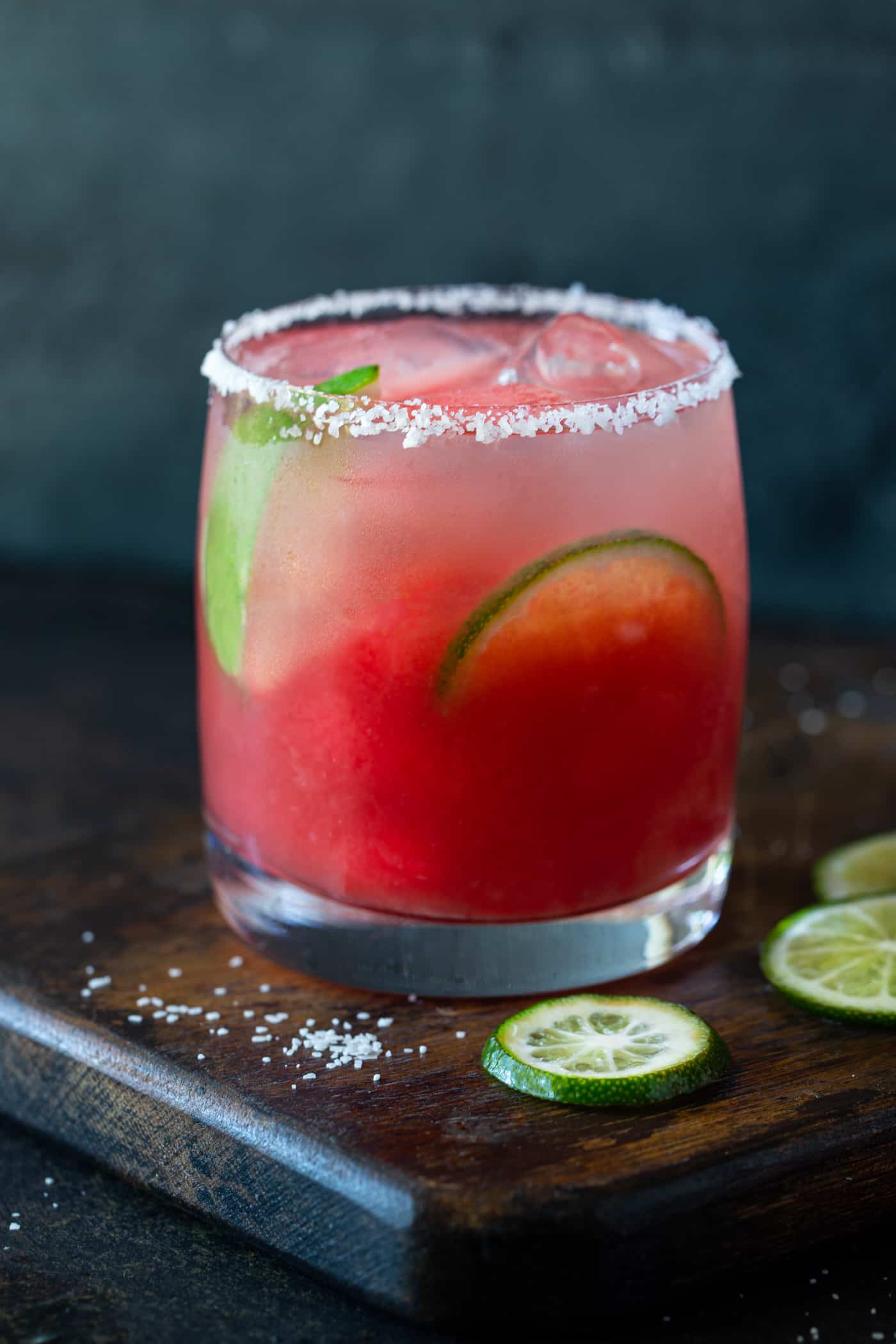 A watermelon margarita served in a lowball glass with salted rim. Garnished with fresh lime wheels and watermelon. 