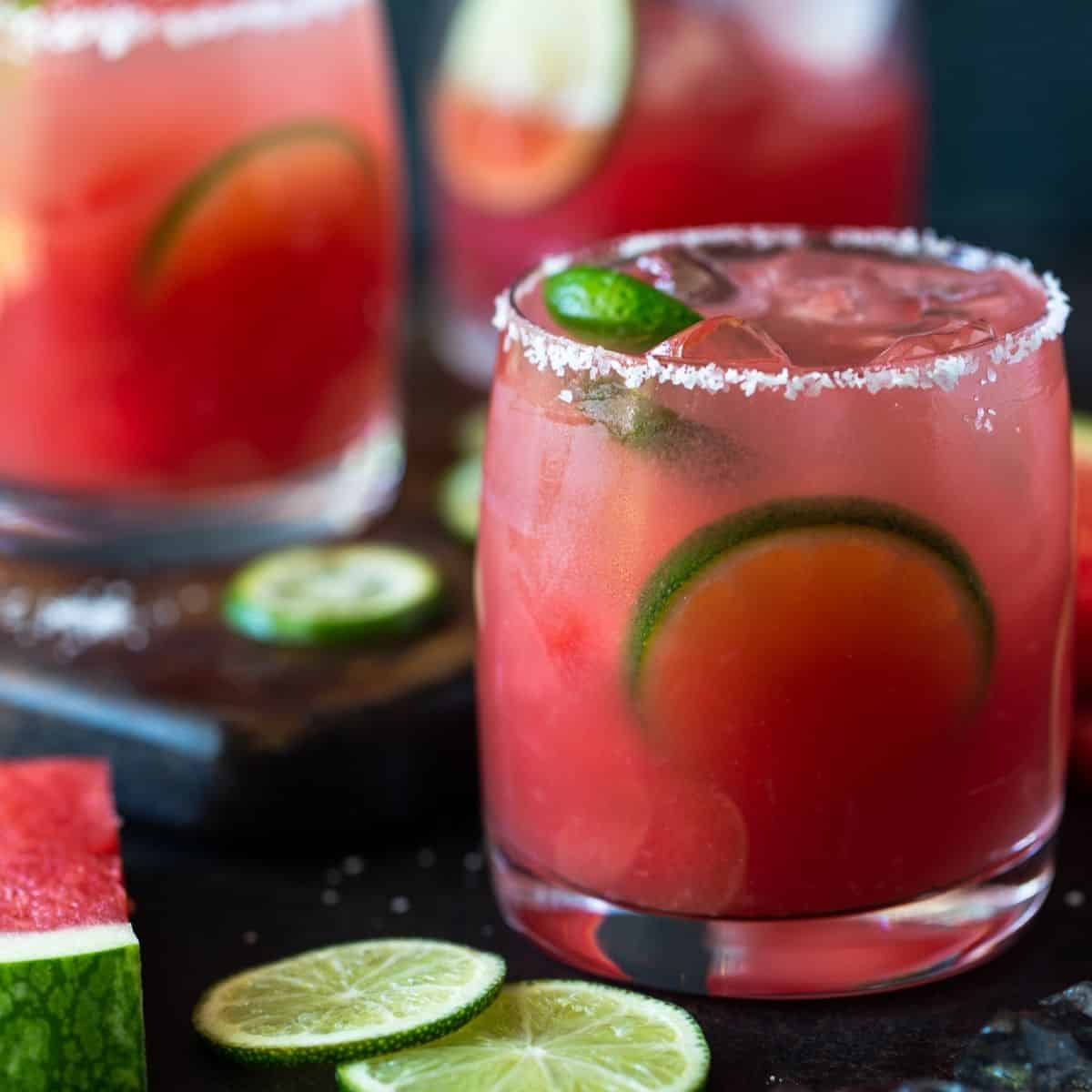 Watermelon margarita in an ice filled glass rimmed with salt and garnished with lime wedges.