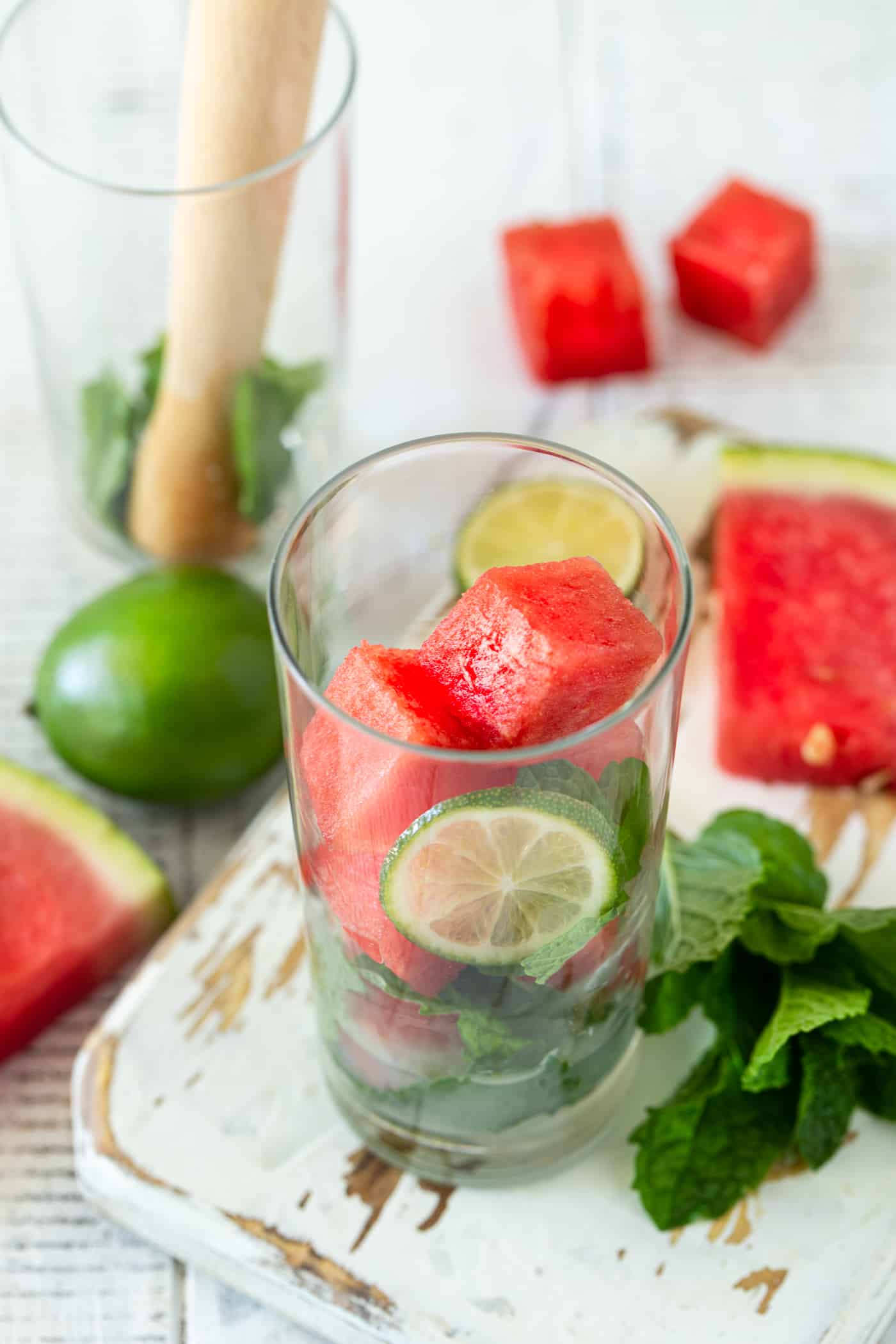 Highball glass filled with watermelon cubes, mint leaves, lime juice and sugar to make a watermelon mojito.