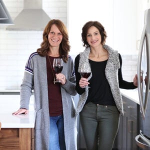 Lisa and Anna holding glasses of wine in test kitchen. 