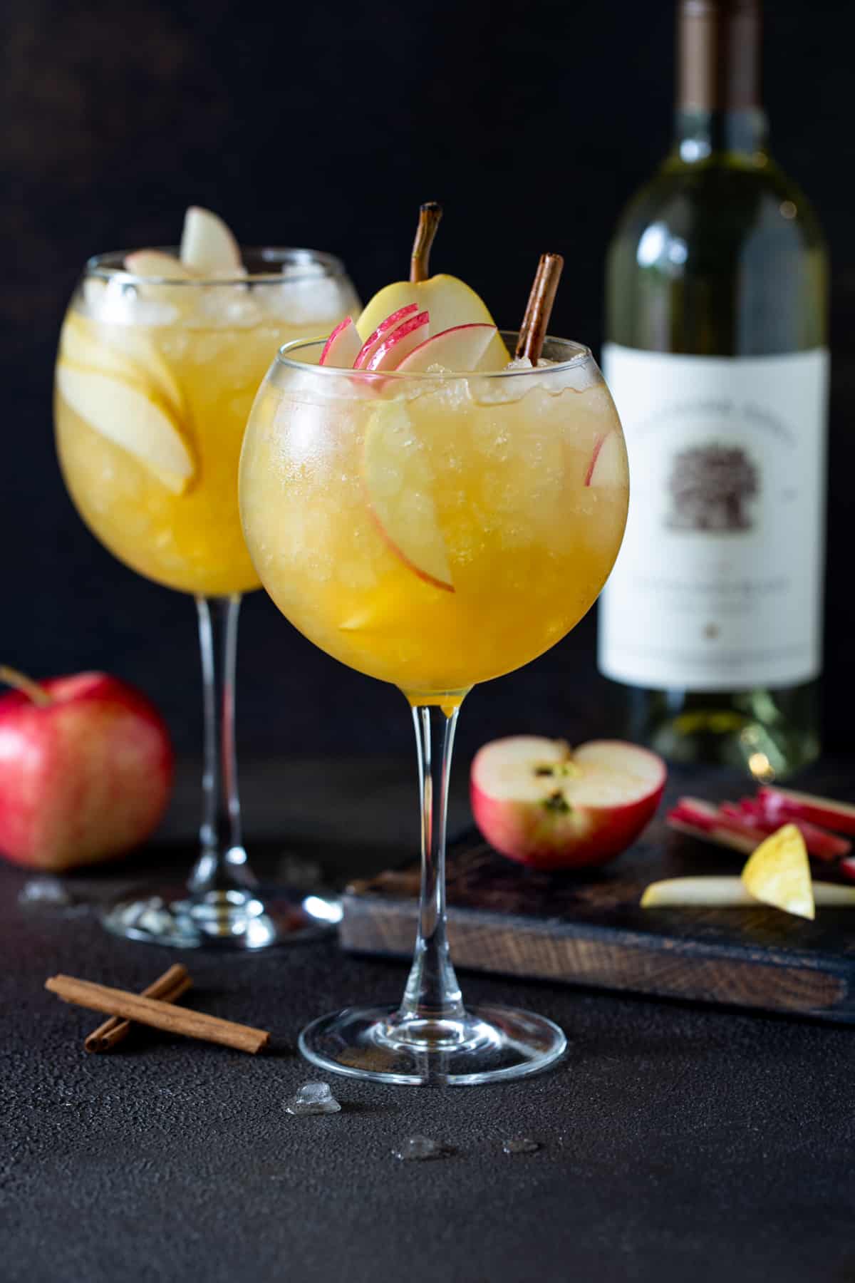 Two balloon wine glasses filled with Apple Cider Sangria. Garnished with fresh apple and pear slices and cinnamon sticks. 