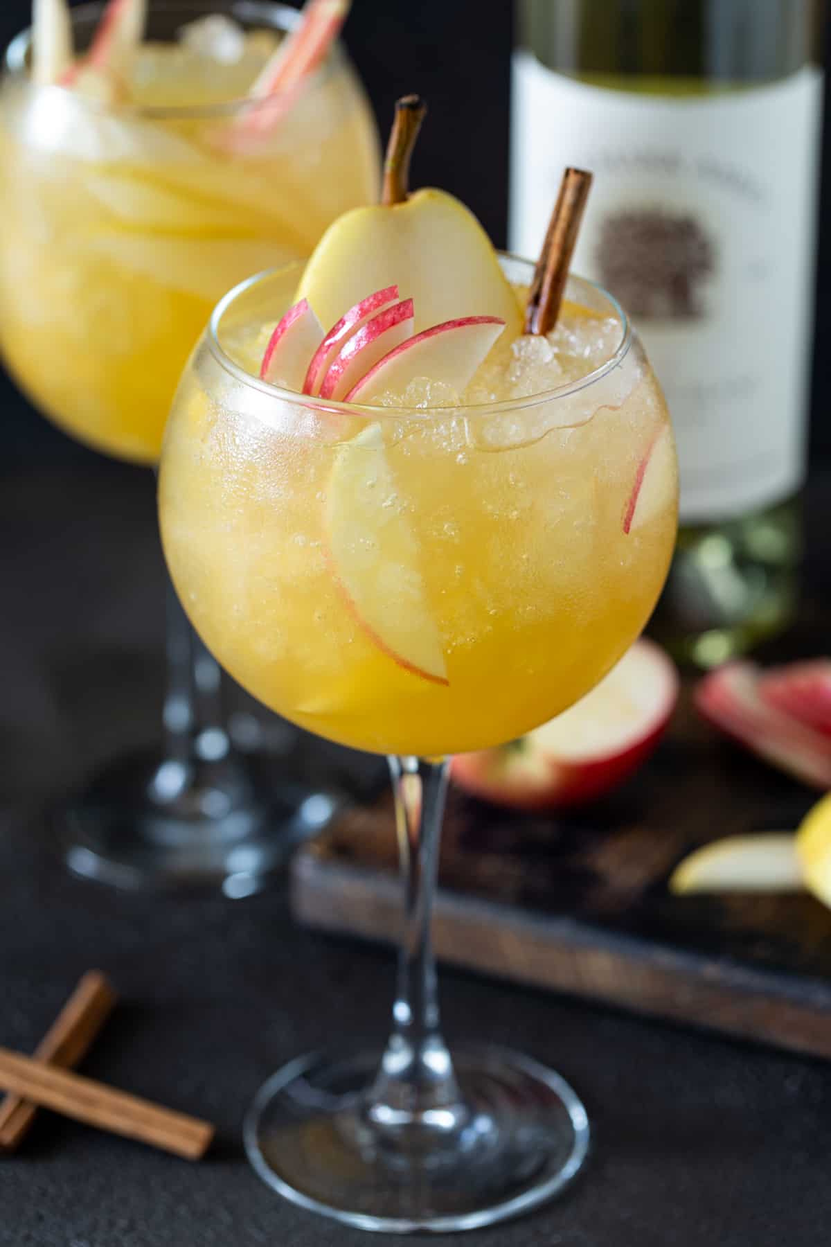 Two balloon wine glasses filled with Apple Cider Sangria. Glasses are garnished with fresh apple and pear slices and cinnamon sticks. 