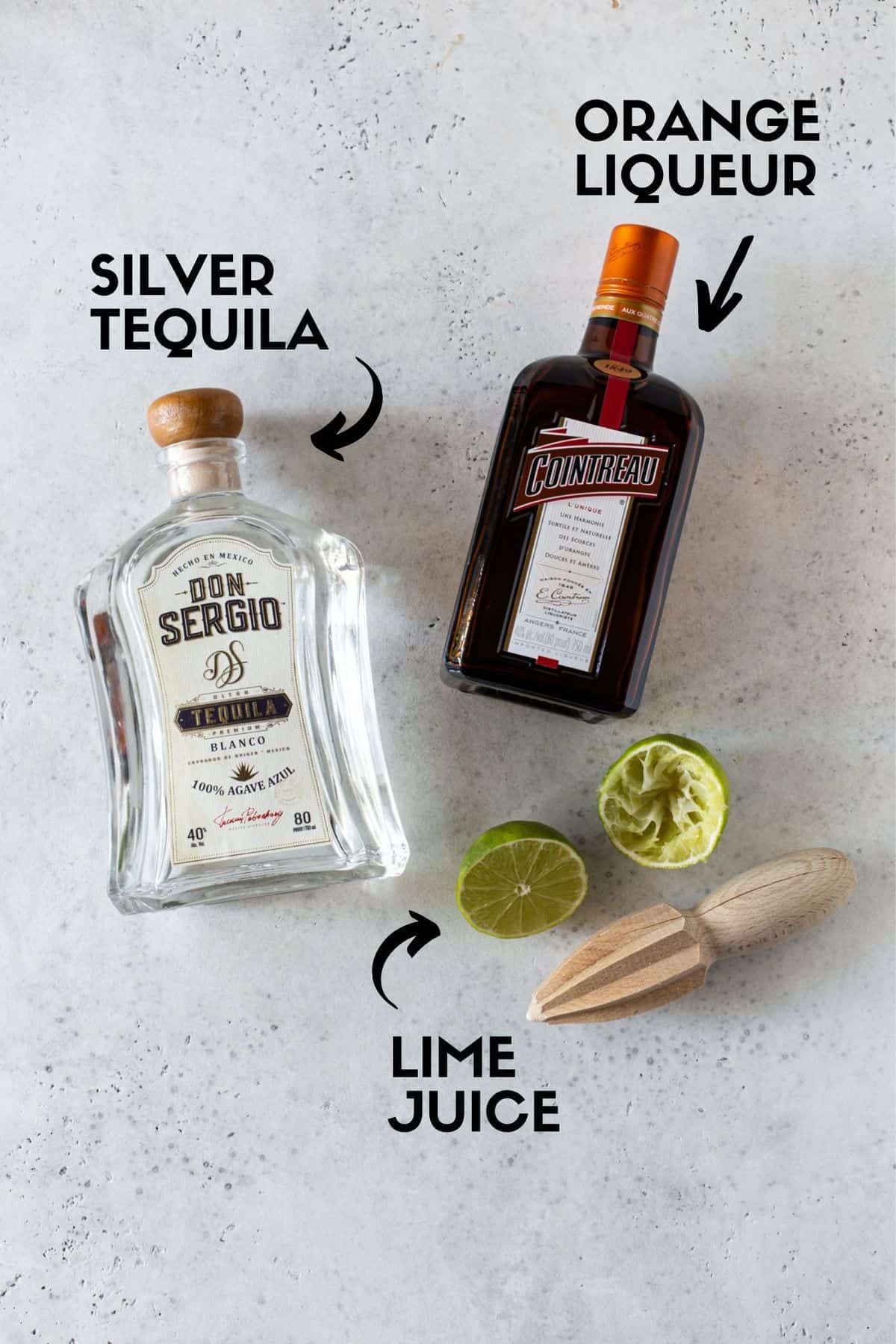 Margarita ingredients including tequila bottle, cointreau bottle and lime half. 