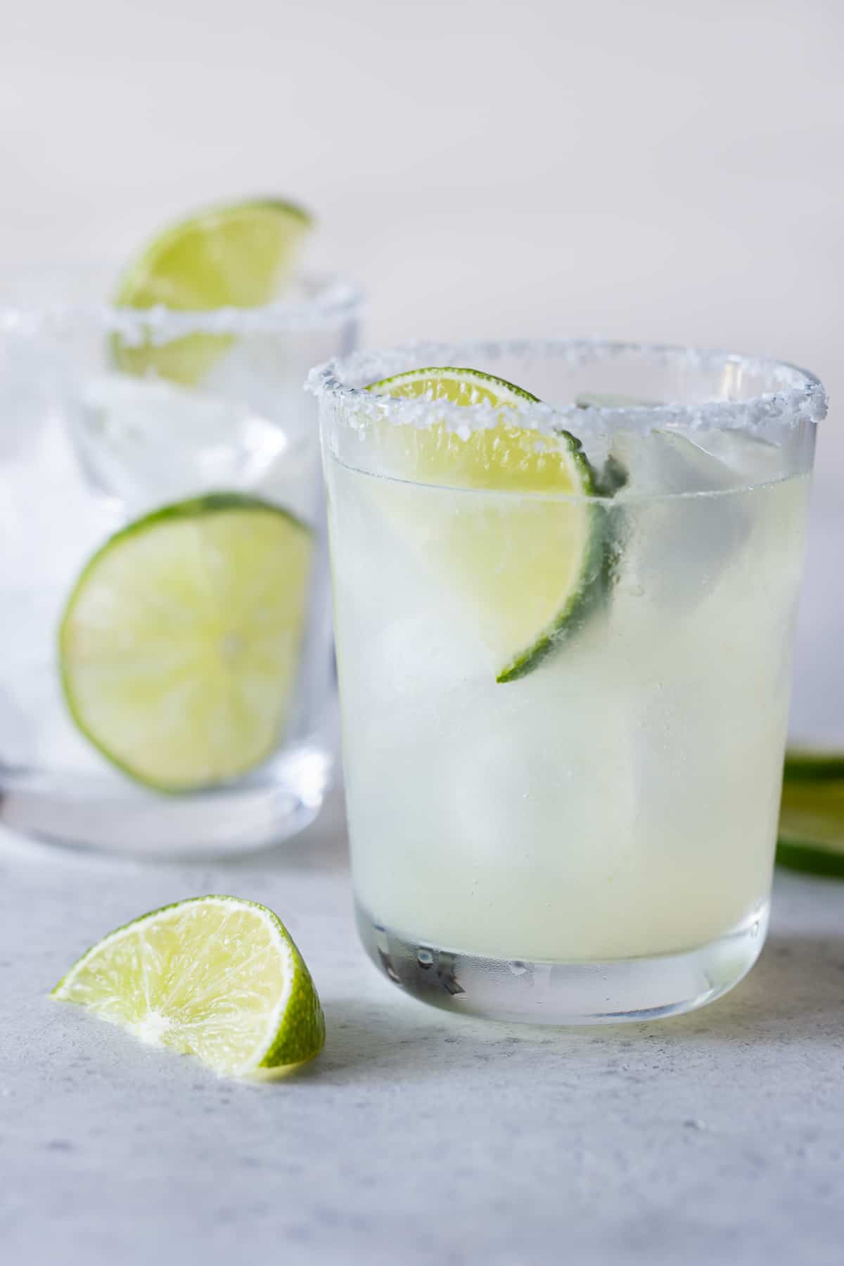 2 low ball glasses filled with ice and margaritas with a salted rim