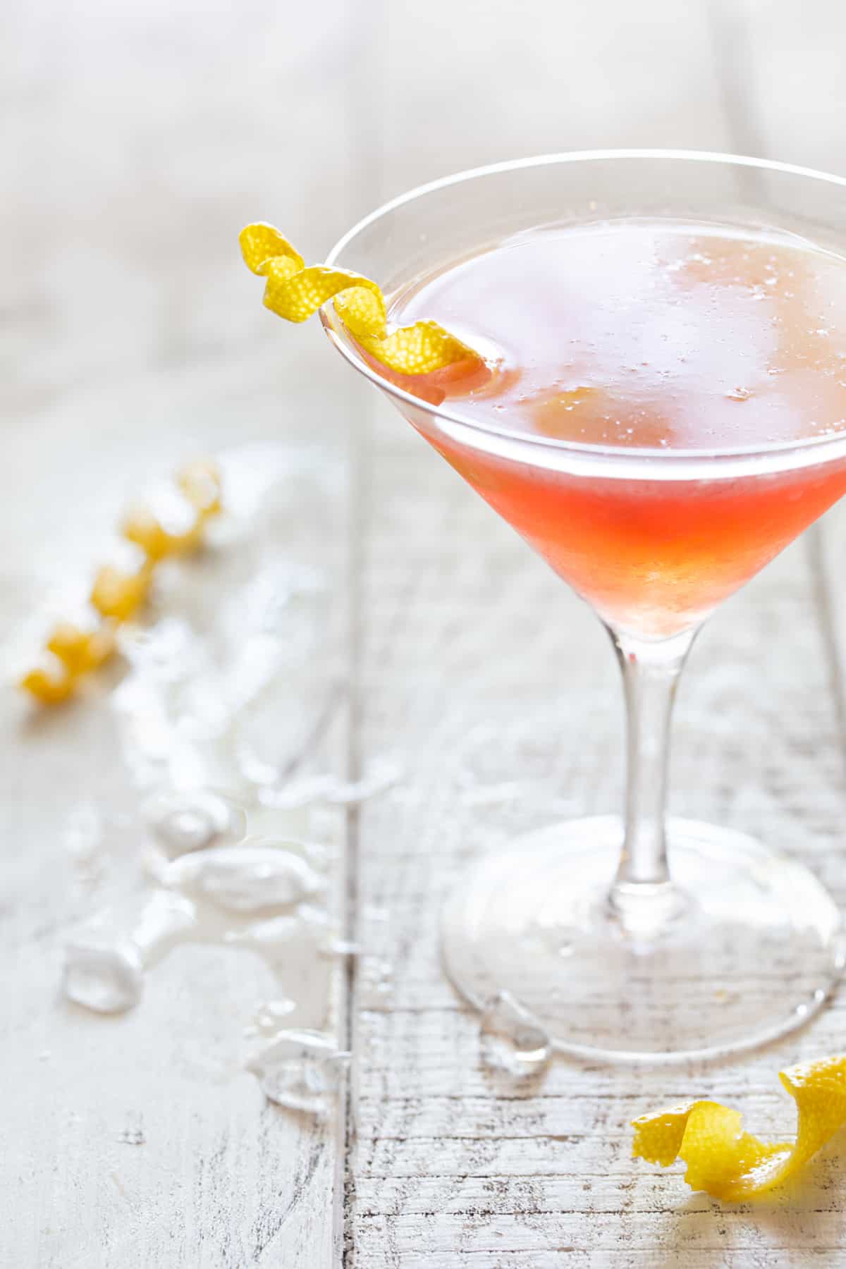 tall martini glass filled with cosmo on a white background with crushed ice and a lemon twist.