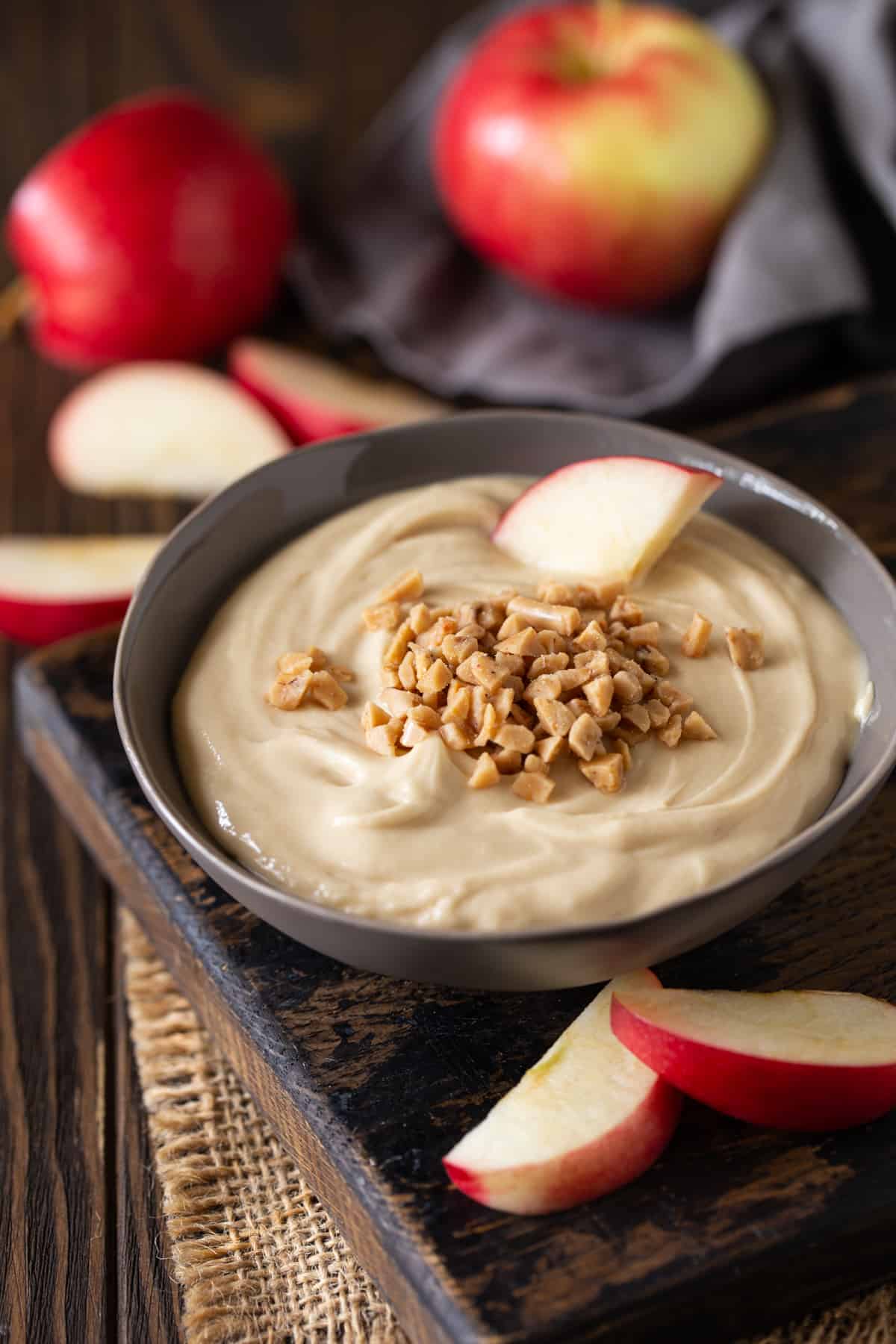 ¾ angle of gray bowl filled with dip, topped with toffee bits and apple slices