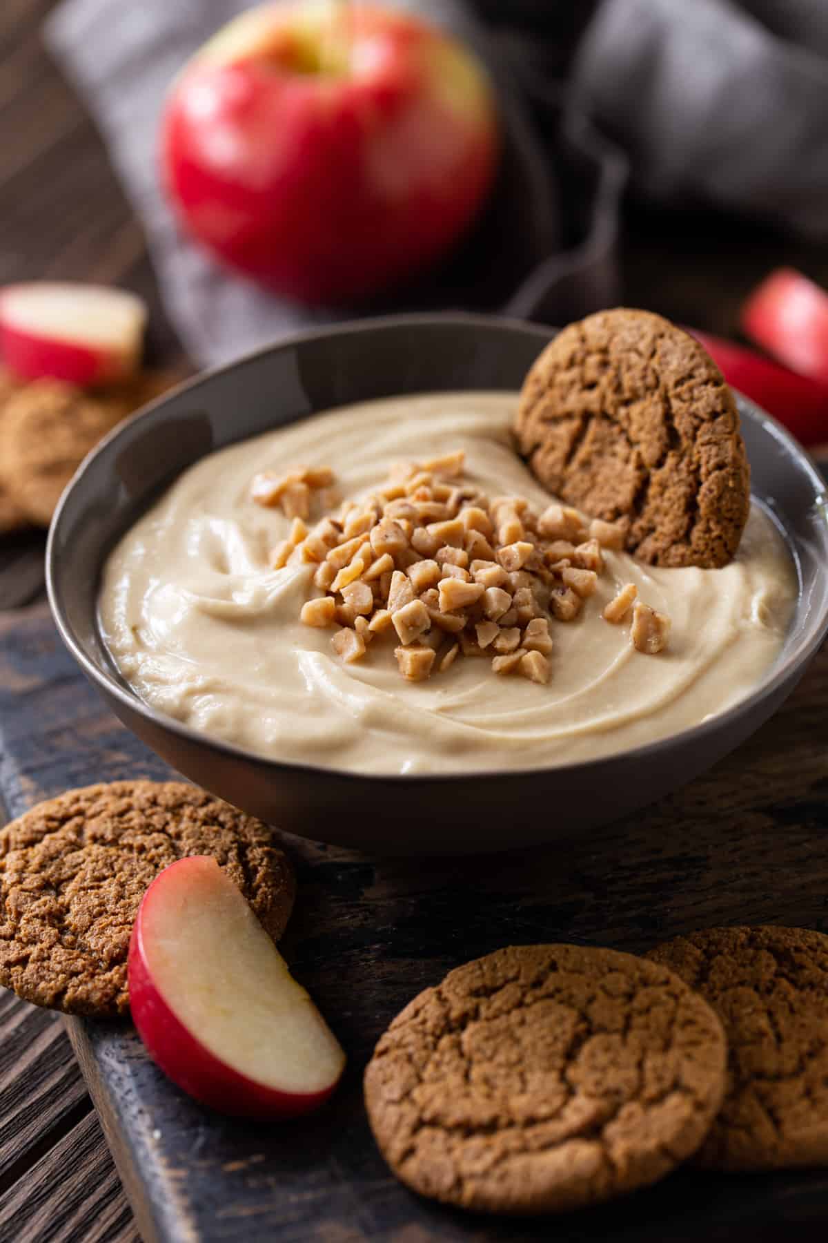 ginger snaps and toffee bits on top of dip in gray bowl on dark background