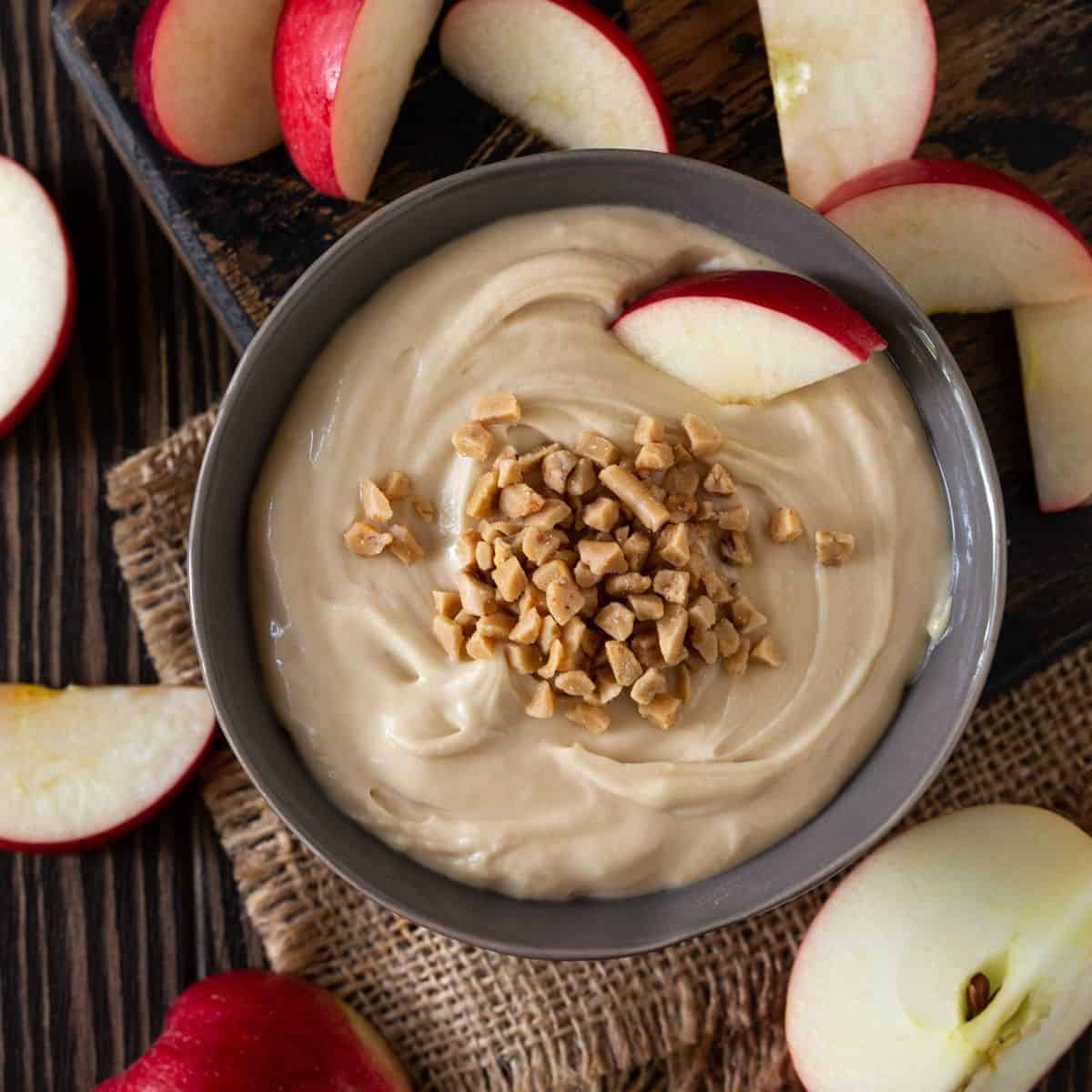 A bowl filled with Apple cream cheese dip and sliced apples on plate.