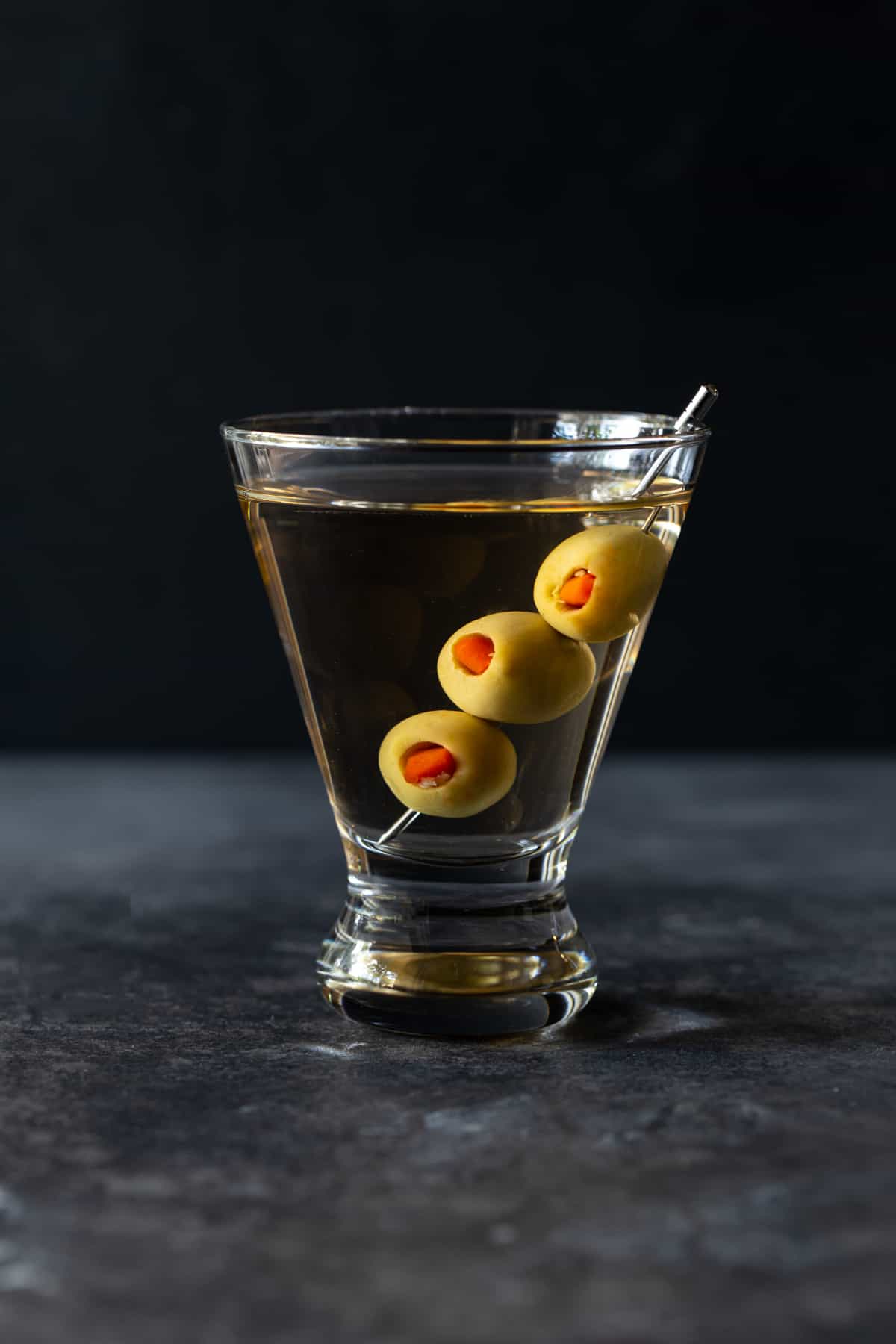 single martini glass filled with gin and olives on a skewer.