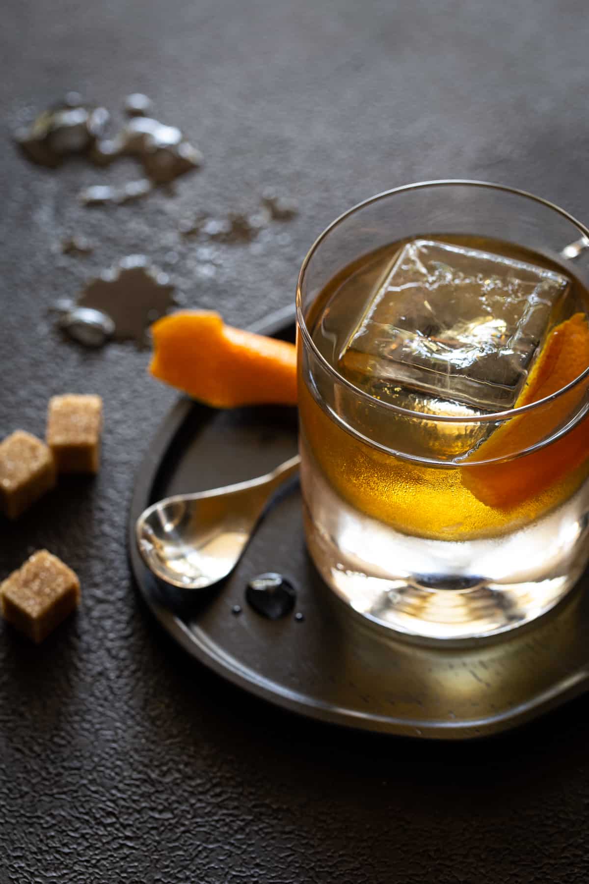 An old fashioned in a lowball glass with a large ice cube and an orange  peel