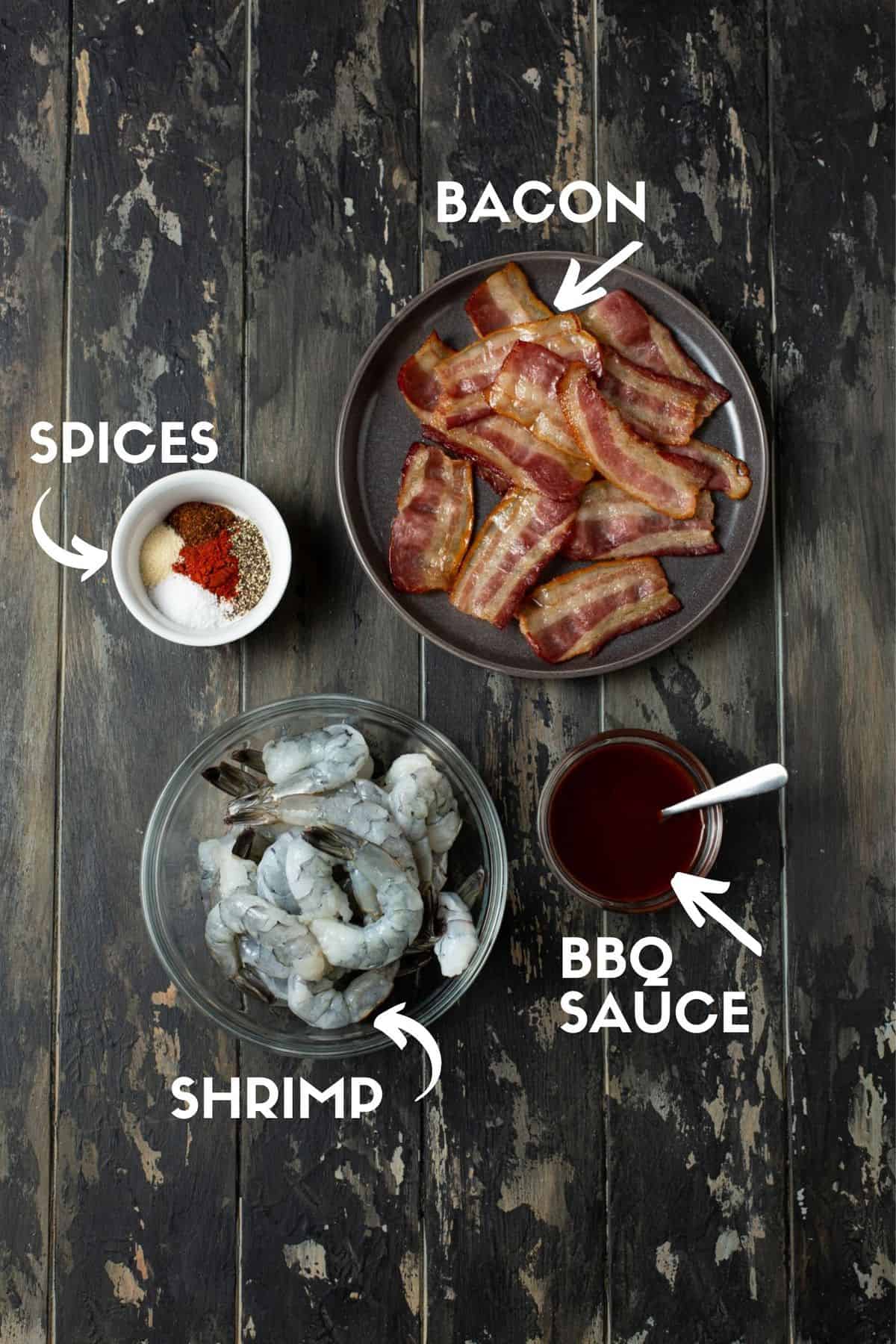 bacon on a plate, spices in a bowl, shrimp in a bowl and small bowl of BBQ sauce.
