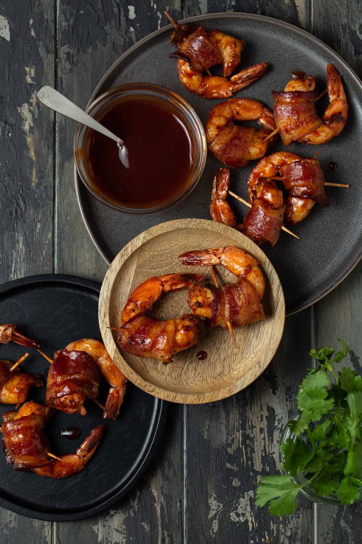 three plates filled with shrimp with a bowl of barbecue sauce and cilantro for garnish.