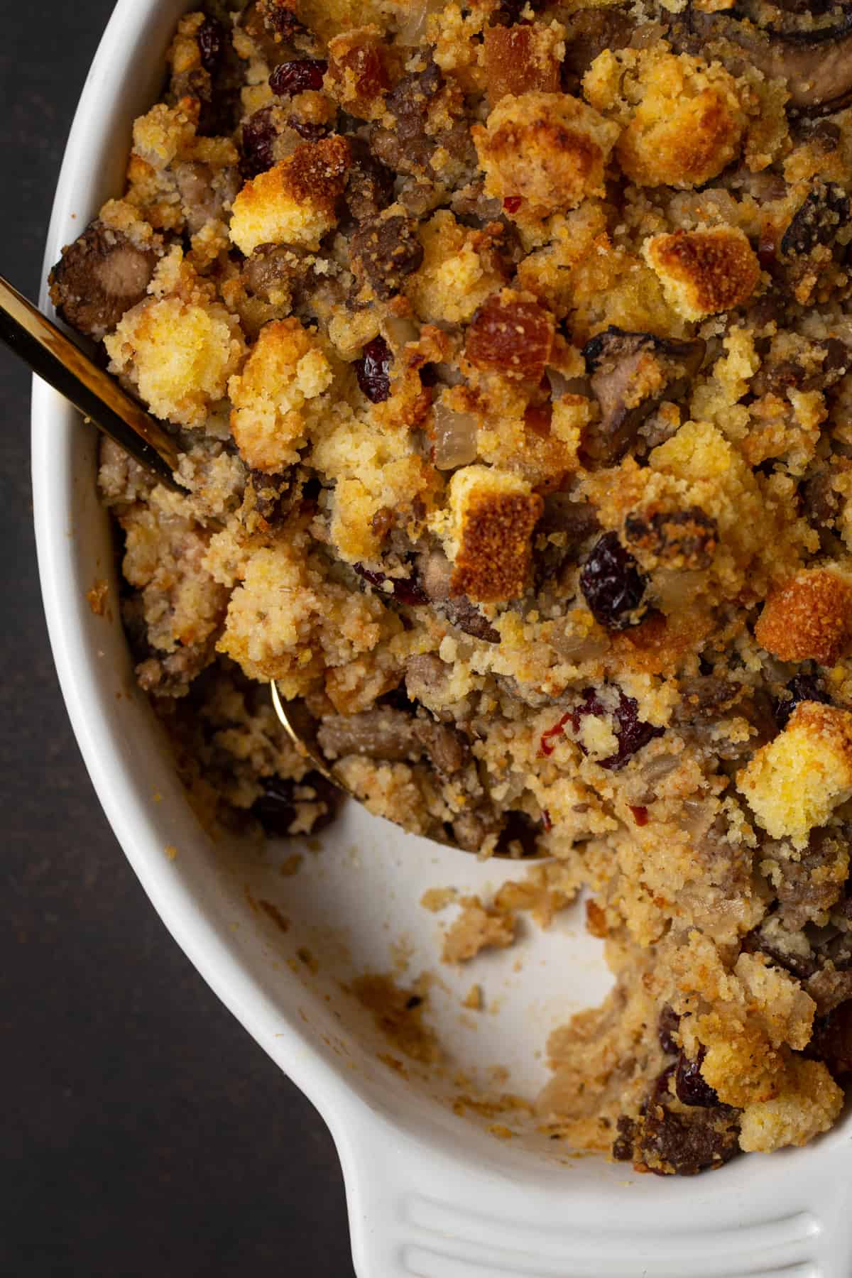 Cornbread stuffing in a white baking dish with gold spoon