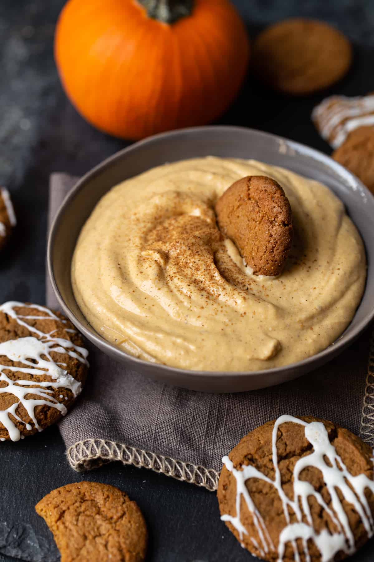 Dip dusted with pumpkin pie spice in a gray bowl with cookies placed in dip