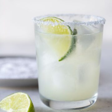 single low ball glass filled with margarita with a salted rim and a lime wedge