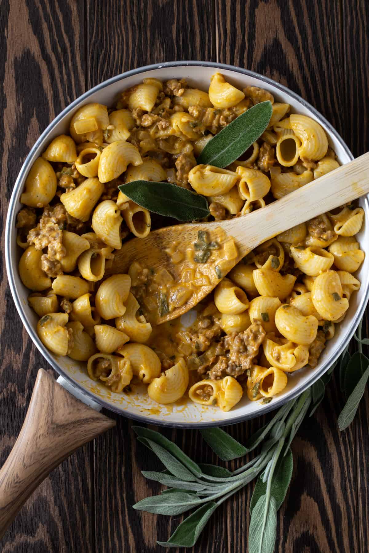 Skillet filled with pumpkin pasta, sausage and sage leaves