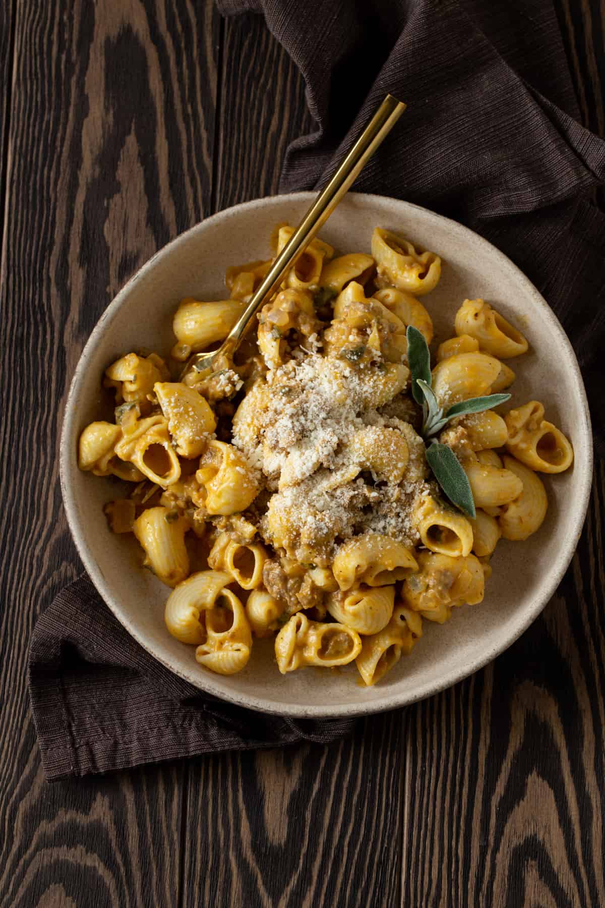 Bowl of pumpkin pasta with sausage, sage and grated parmesan with gold spoon