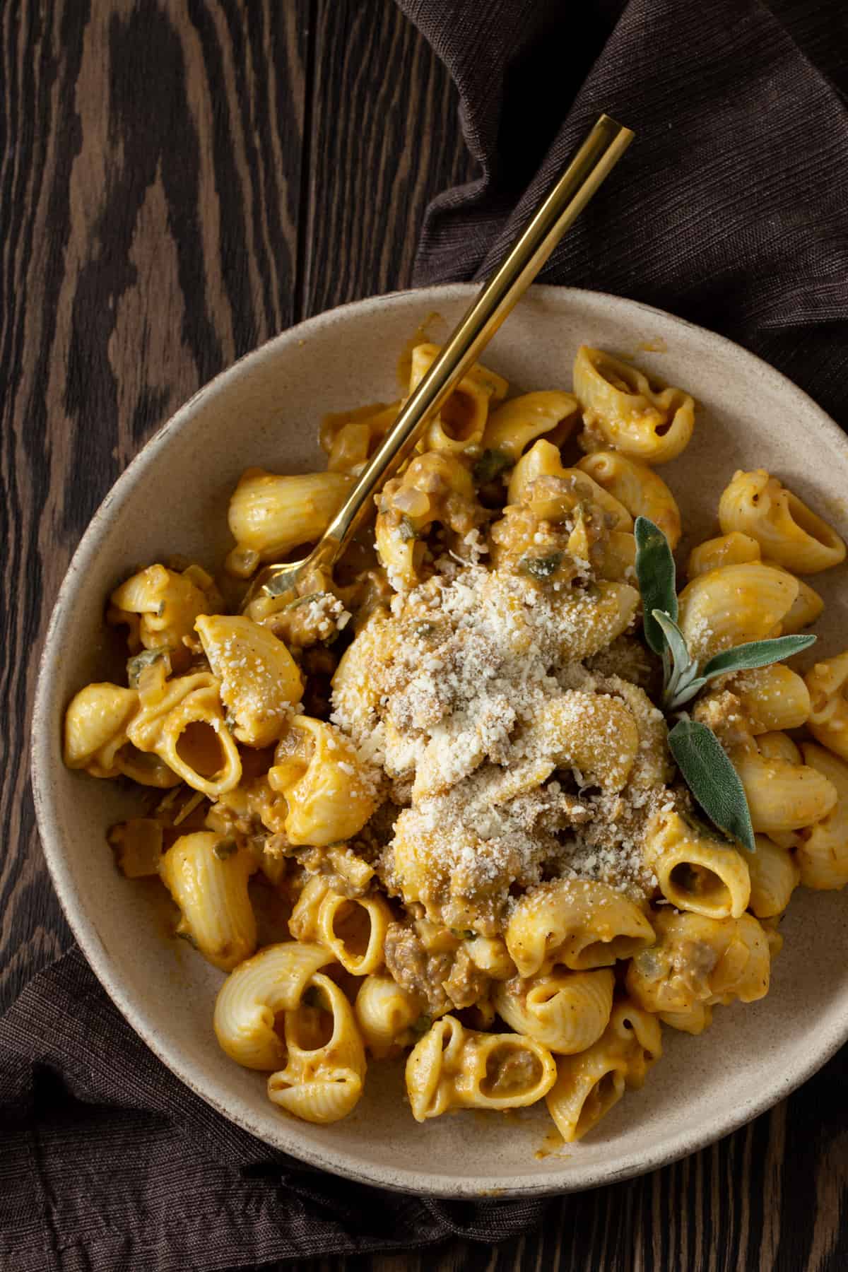 Pumpkin and sausage pasta in a bowl with a gold spoon.
