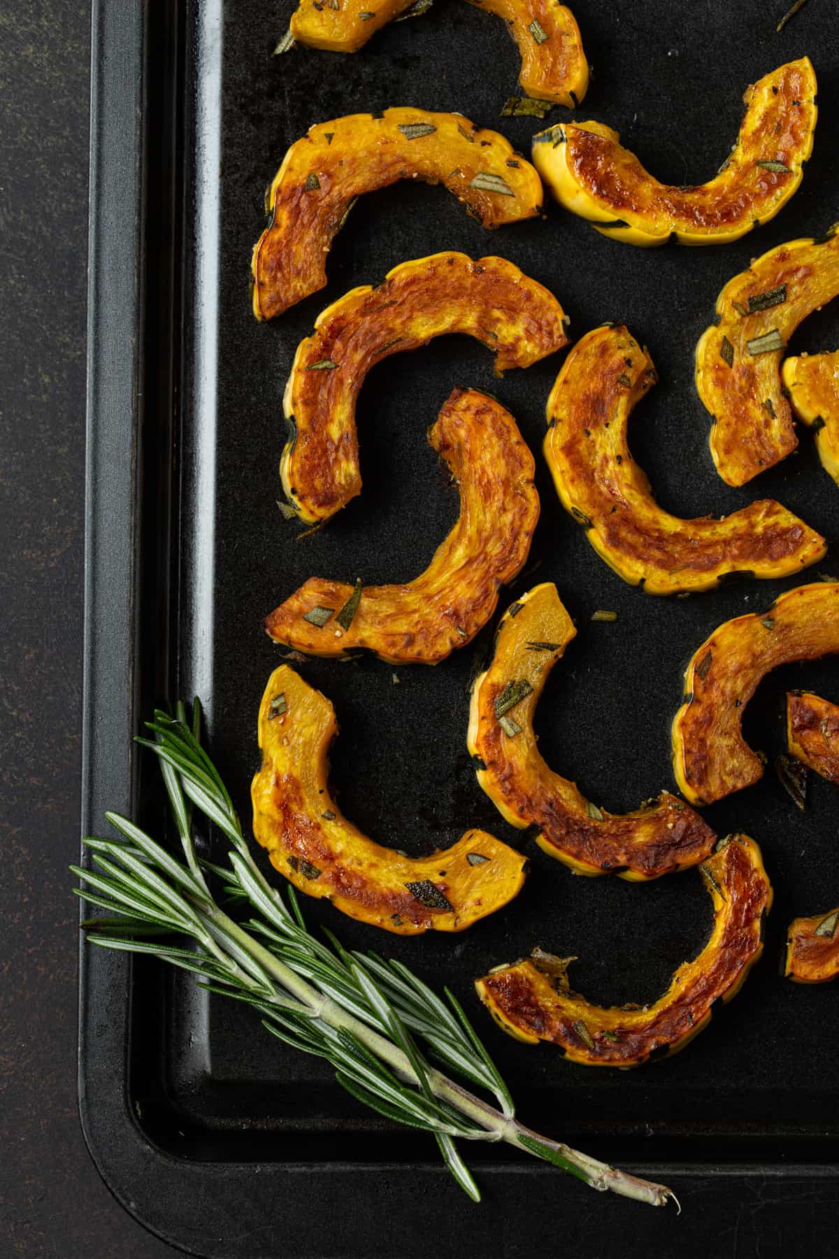 roasted squash pieces on a dark sheet pan with fresh rosemary.