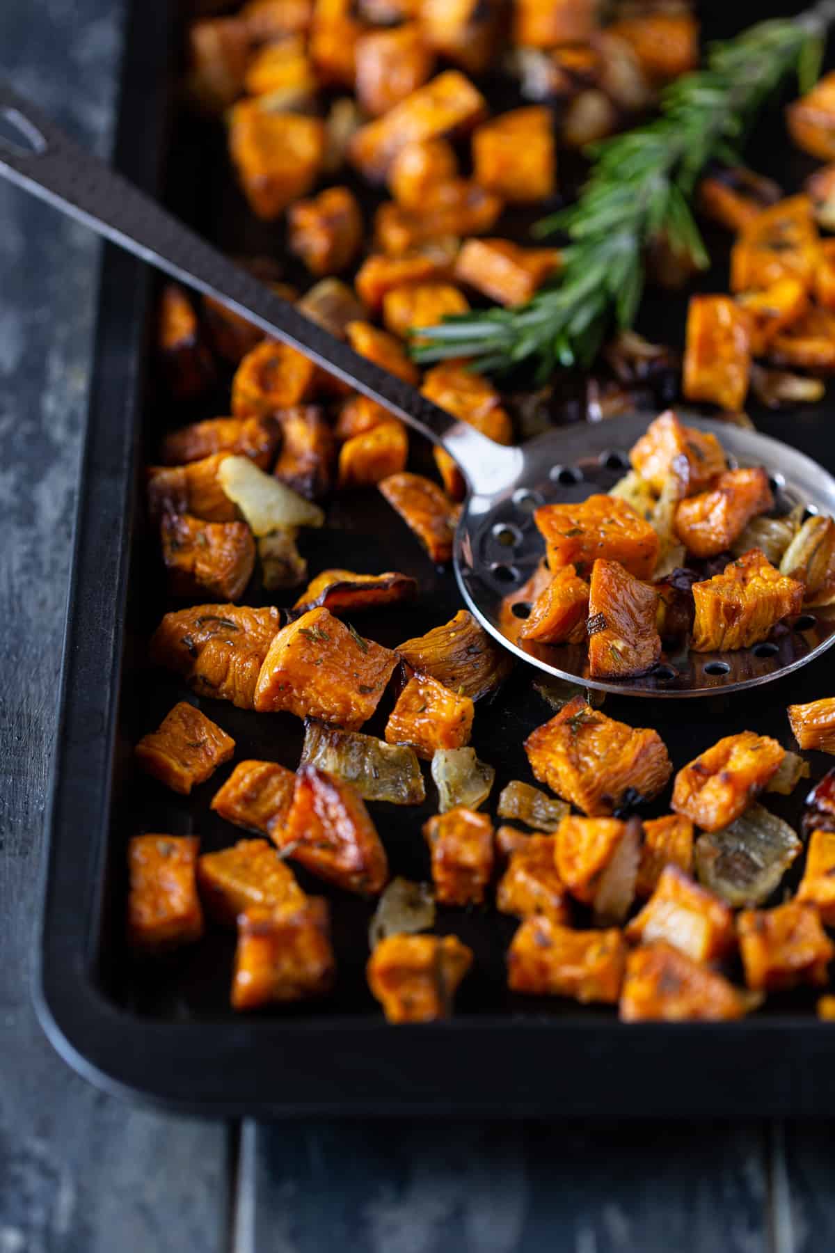 Roasted potatoes and onions on a dark sheet pan.