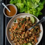 chopped chicken filling for lettuce wraps , bowl of peanut sauce and lettuce cups on black tray.