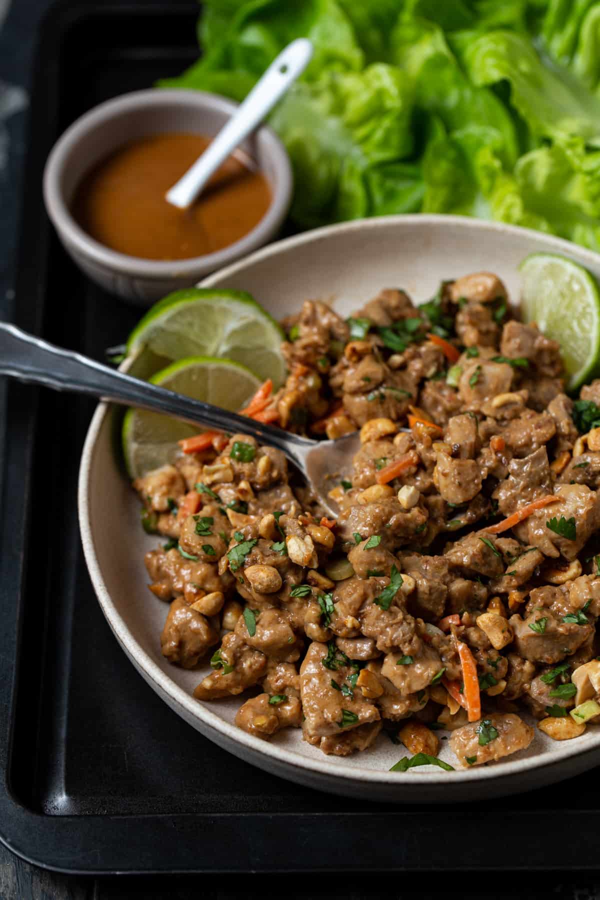 chopped chicken, cilantro carrots and peanuts in a peanut sauce on a gray plate.